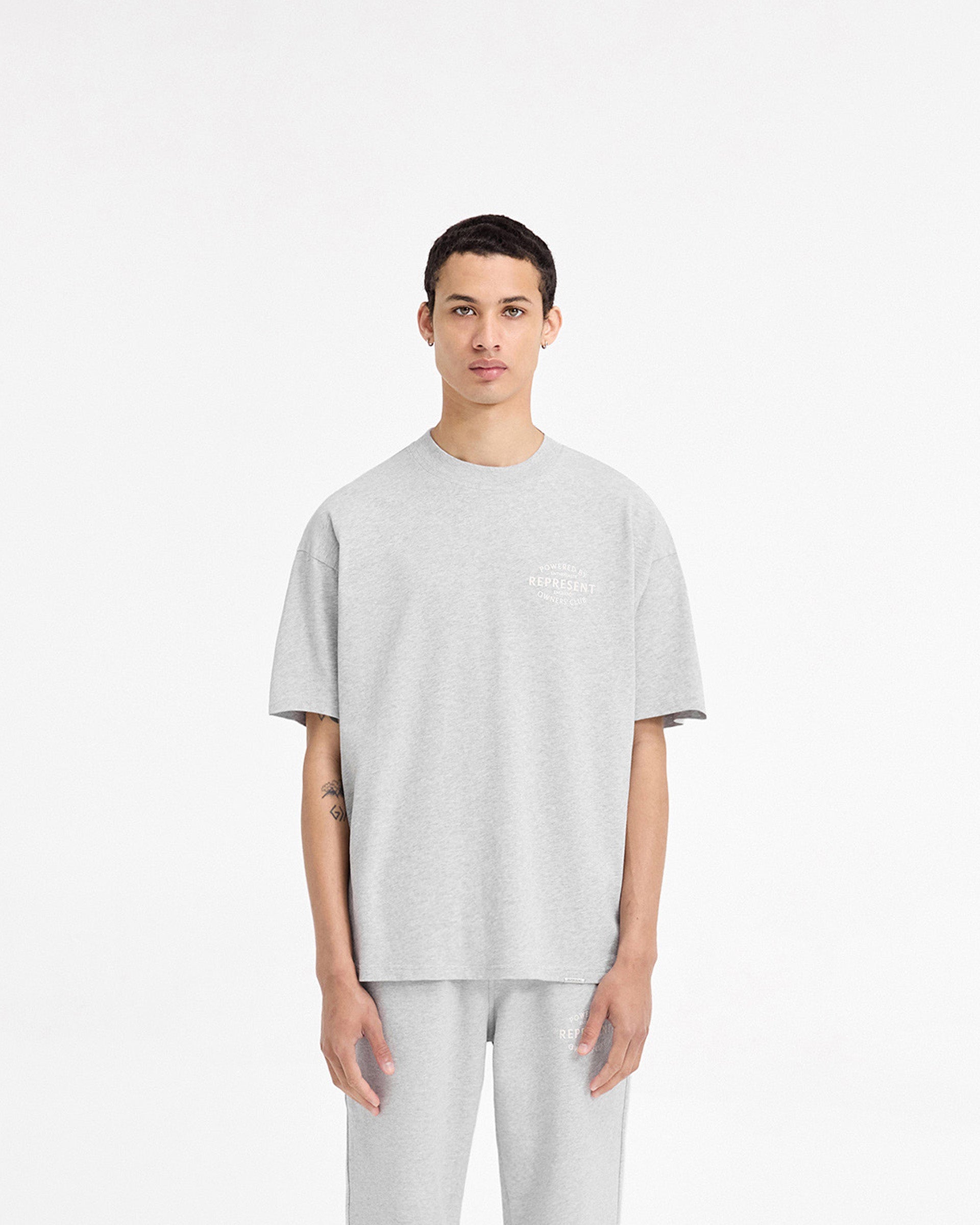 Man wearing a grey t-shirt on a plain white background | Represent Owners Club Stamp T-Shirt in Ash Grey | Slightly oversized fit t-shirt with high build branding | Owners Club T-Shirts | Represent Clo
