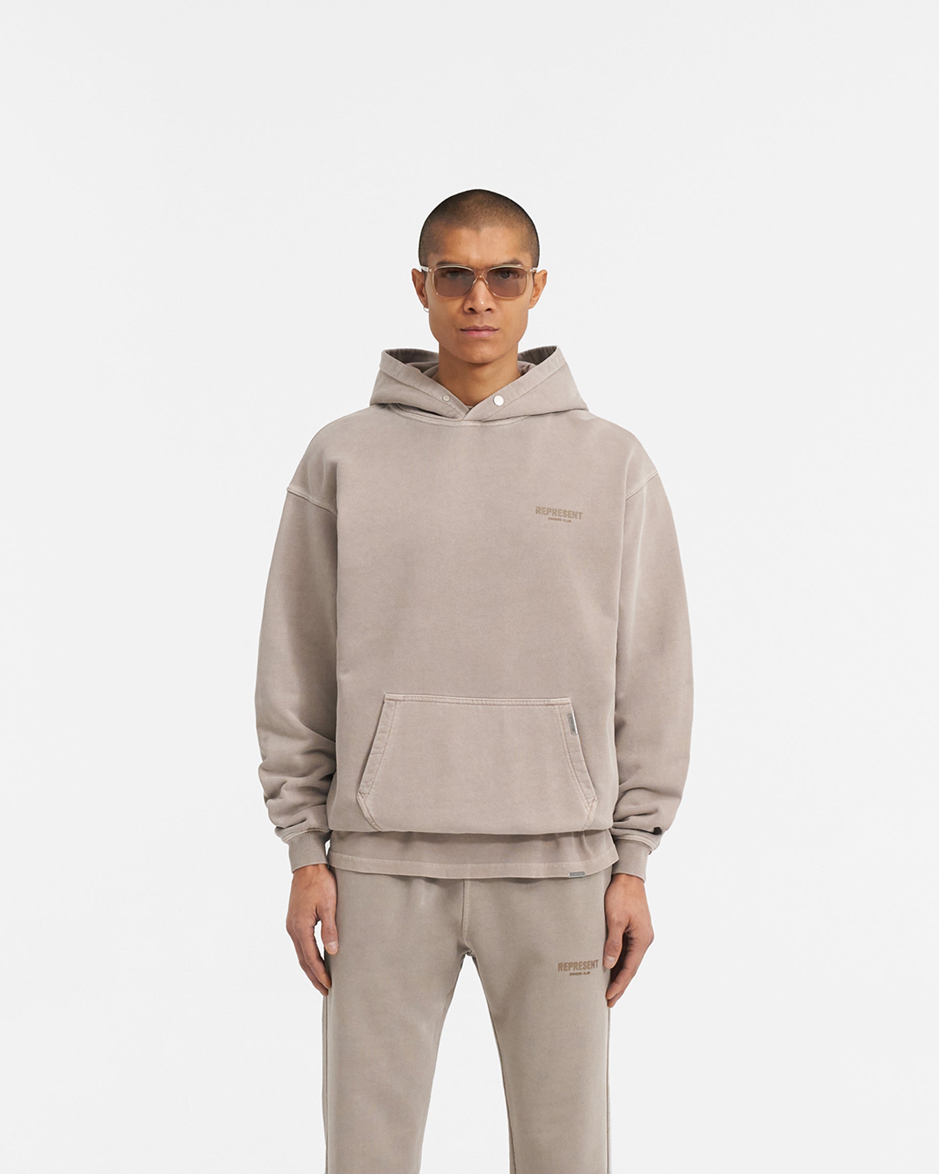 Man wearing an oversized mushroom hoodie on a plain white background | Represent Owners Club Hoodie in Mushroom | Heavy weight jersey cotton hoodie with ribbed trims and Cobrax popper | Owners Club Hoodies | Represent Clo