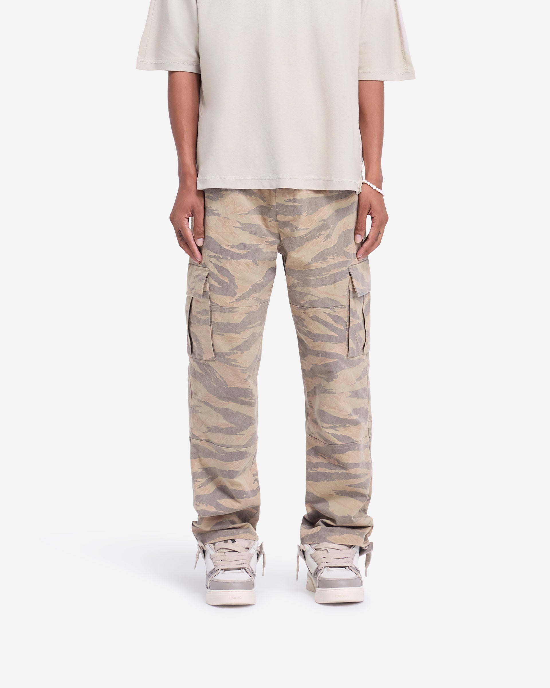 Man wearing camo cargo pants on a plain white background | Cargo Pant in Camo | Regular fit cargo pants with flap pockets and metal bar detailing | FW24 Pants | Represent Clo