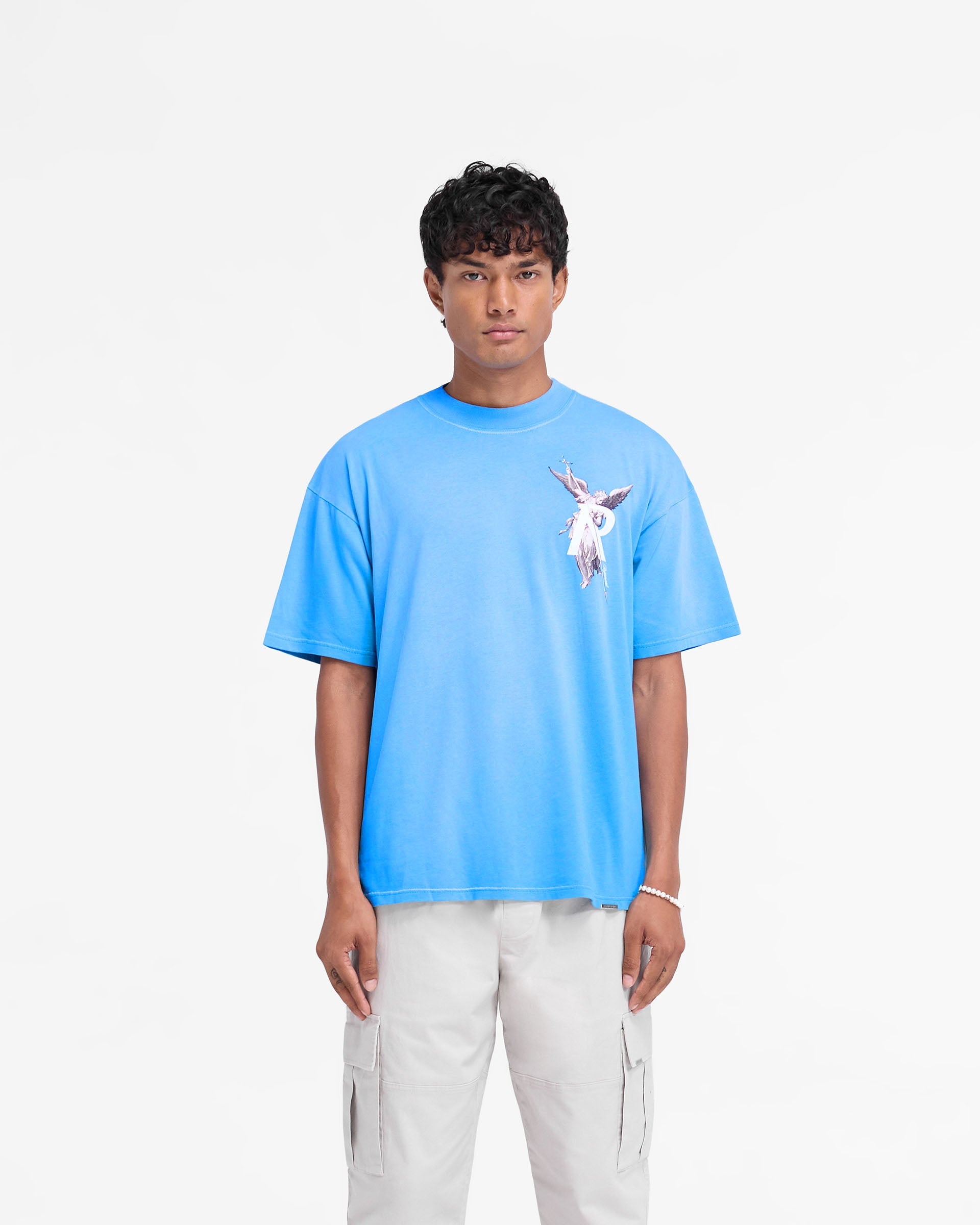 Man wearing a slightly oversized electric blue t-shirt on a plain white background | Archangel T-Shirt in Electric Blue | T-shirt with high density graphic and sun fade wash | FW24 T-Shirts | Represent Clo