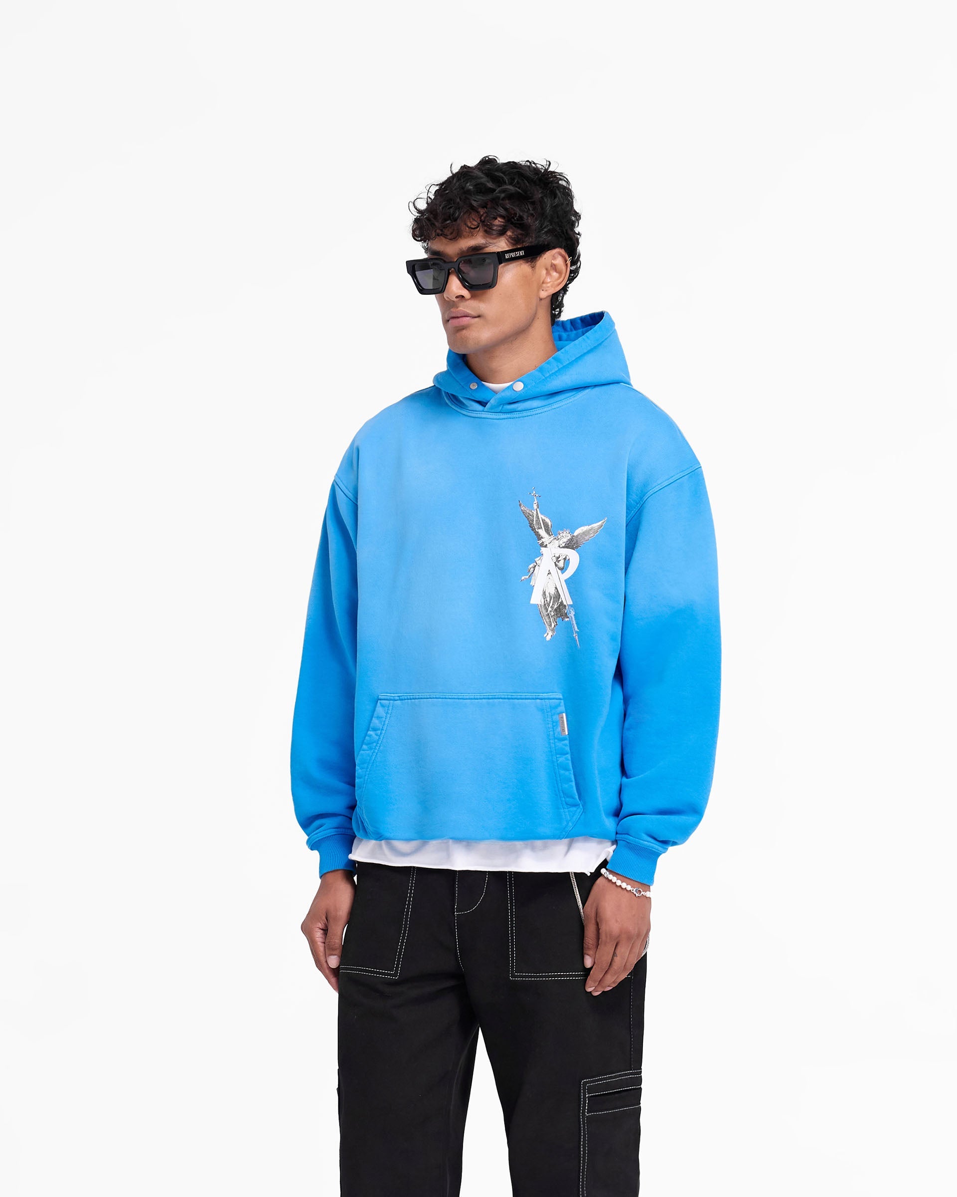 Man wearing an oversized electric blue hoodie on a plain white background | Archangel Hoodie in Electric Blue | Hoodie with ribbed hems and high density graphic | FW24 Hoodies | Represent Clo