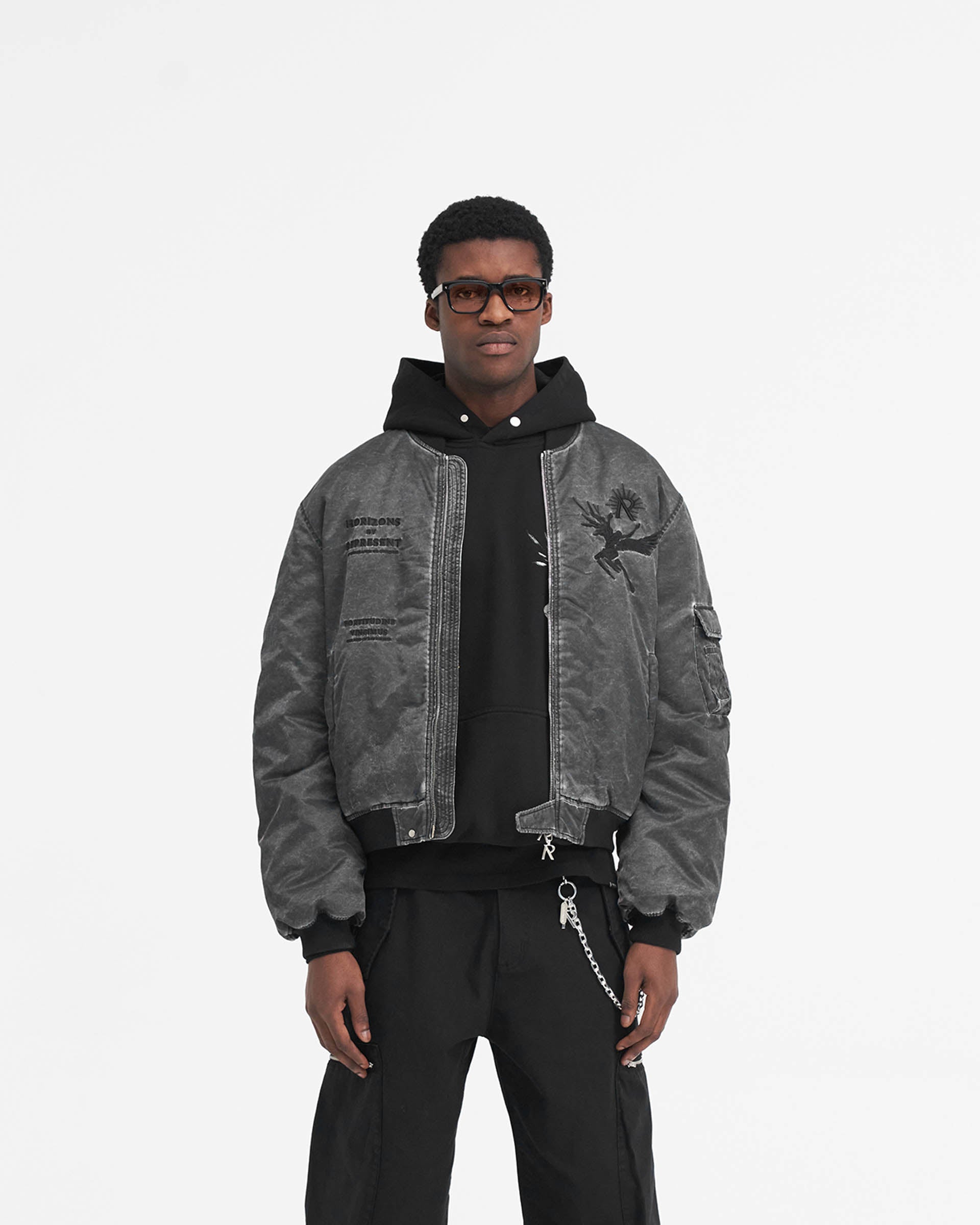 Man wearing a black bomber jacket on a plain white background | Icarus Flight Bomber in Jet Black | Bomber jacket with sleeve gathering and embroidered artwork | SS24 Outerwear | Represent Clo