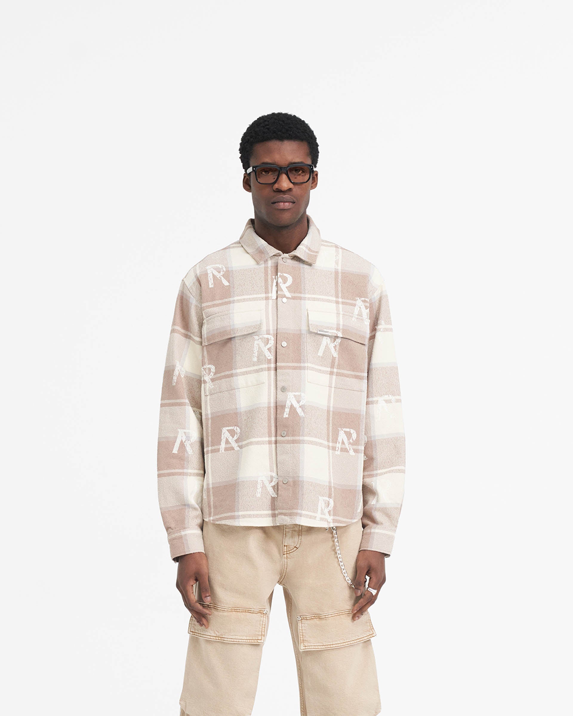Man wearing a brown check flannel shirt on a plain white background | All Over Initial Flannel Shirt in Cashmere | Oversized cotton blend shirt with Cobrax popper fastenings | SS24 Shirts | Represent Clo