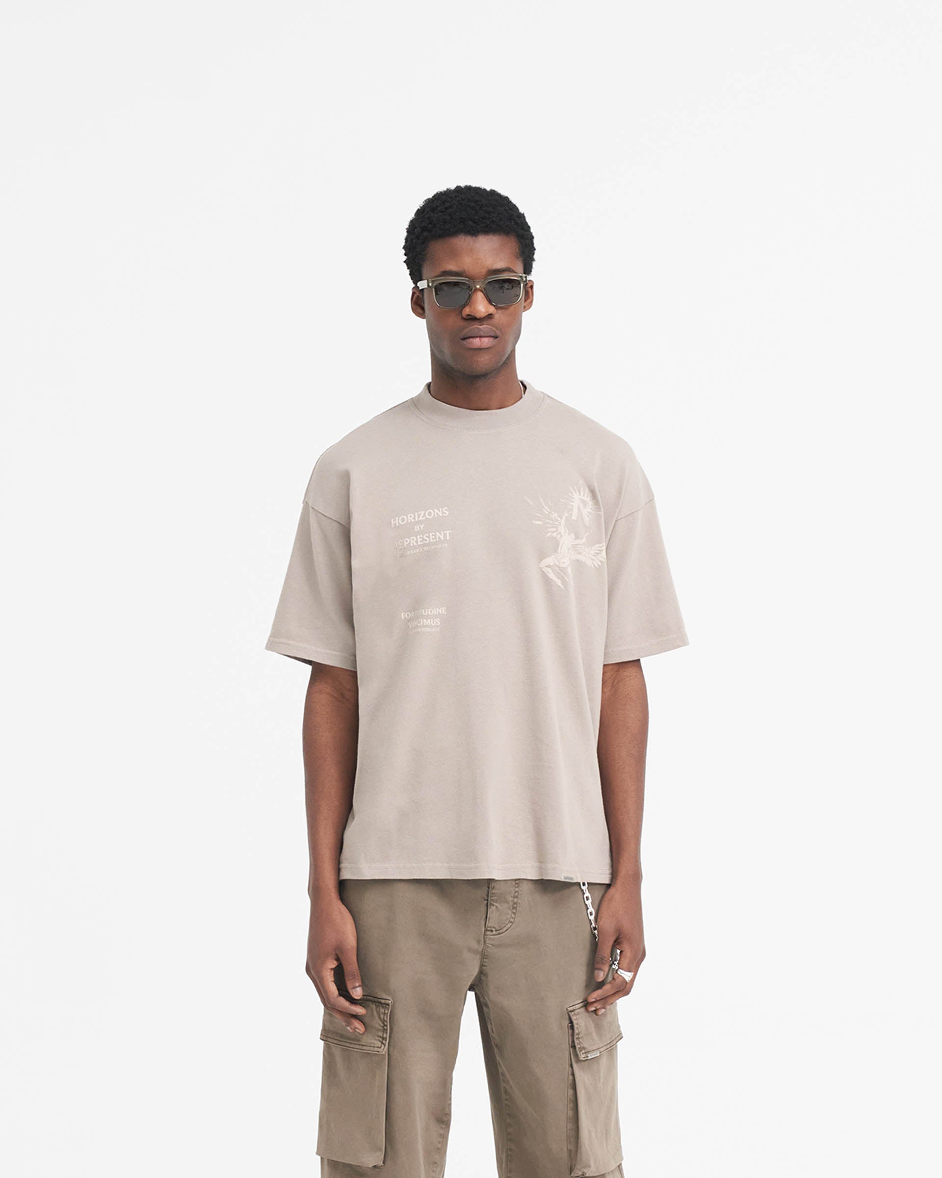 Man wearing an oversized taupe t-shirt on a plain white background | Icarus T-Shirt in Taupe | Medium weight cotton t-shirt with Icarus graphic | SS24 T-Shirts | Represent Clo