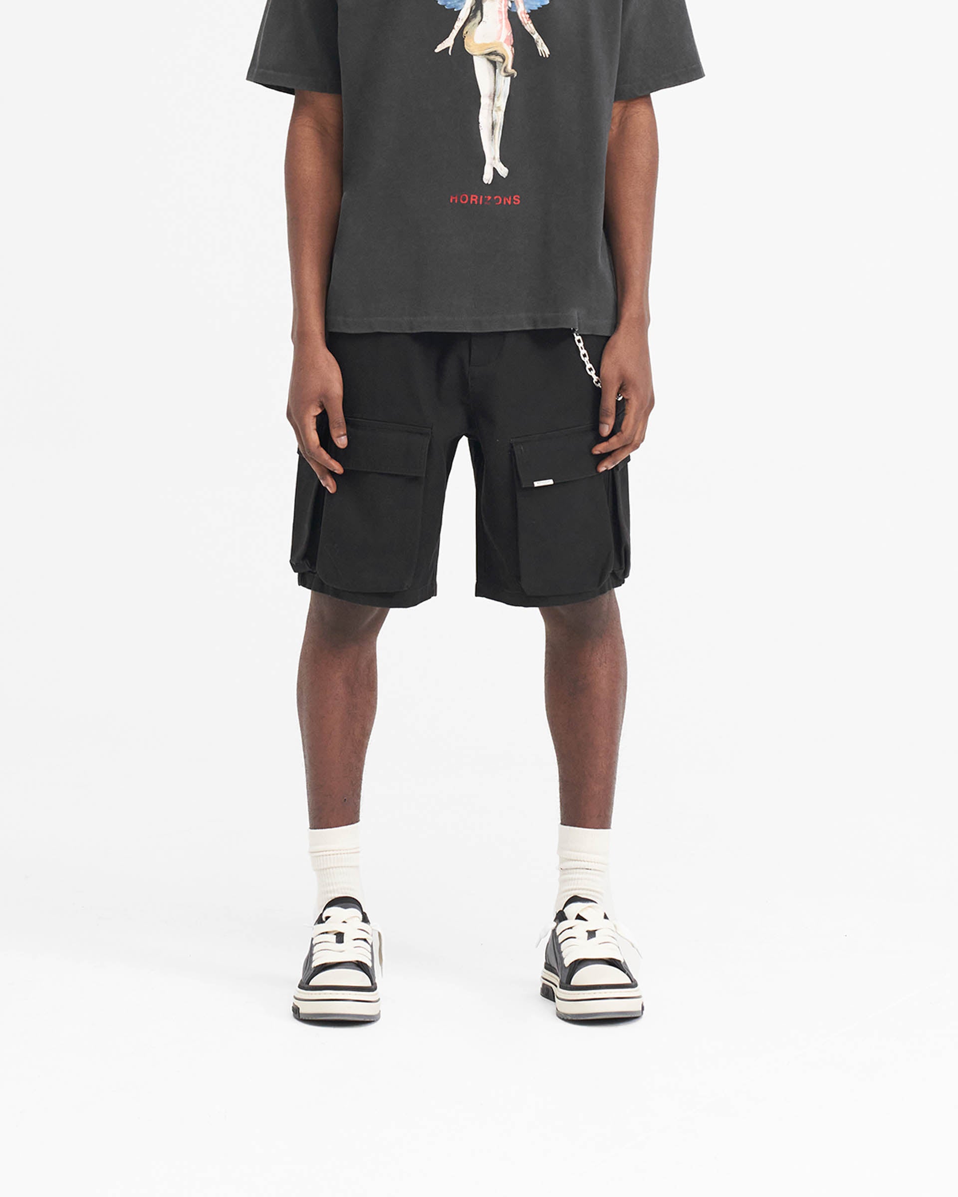 Man wearing black baggy cotton cargo shorts on a plain white background | Baggy Cotton Cargo Short in Black | Baggy fit shorts with 3D pockets | SS24 Shorts | Represent Clo