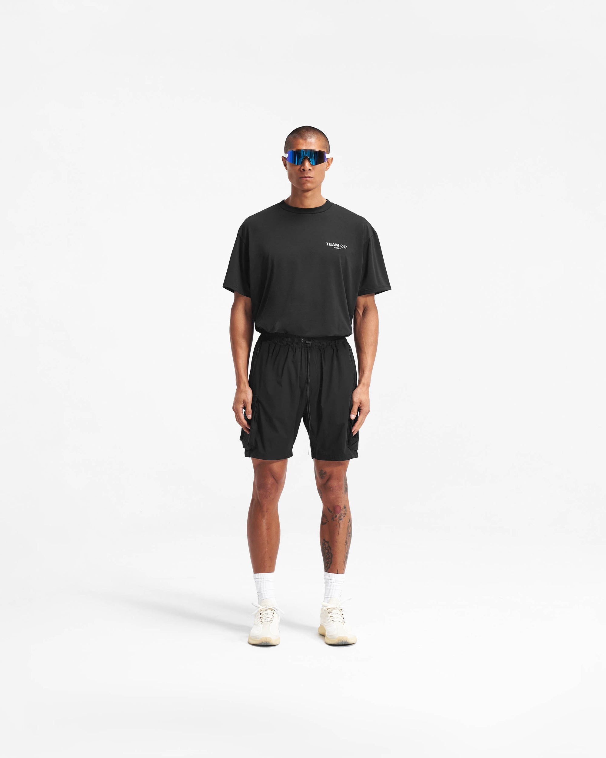 Man wearing black shorts on a plain white background | 247 Shorts in Black | Mens combat shorts with cargo and zip pockets | 247 Shorts | Represent Clo