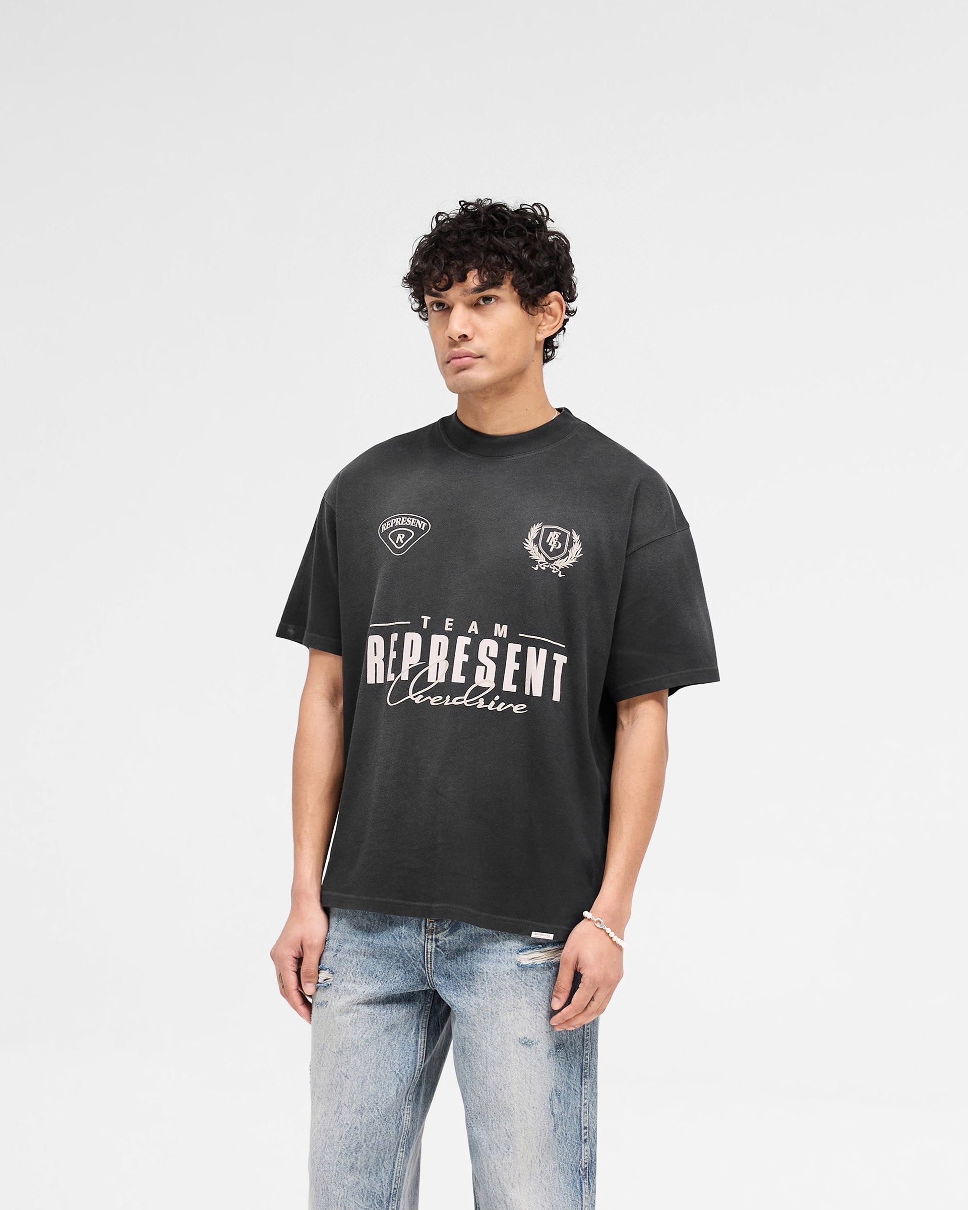 Man wearing a black t-shirt with graphic print on a plain white background | World Championship T-Shirt in Stained Black | Slightly oversized t-shirt with fade out spray | SS25 T-Shirts | Represent Clo