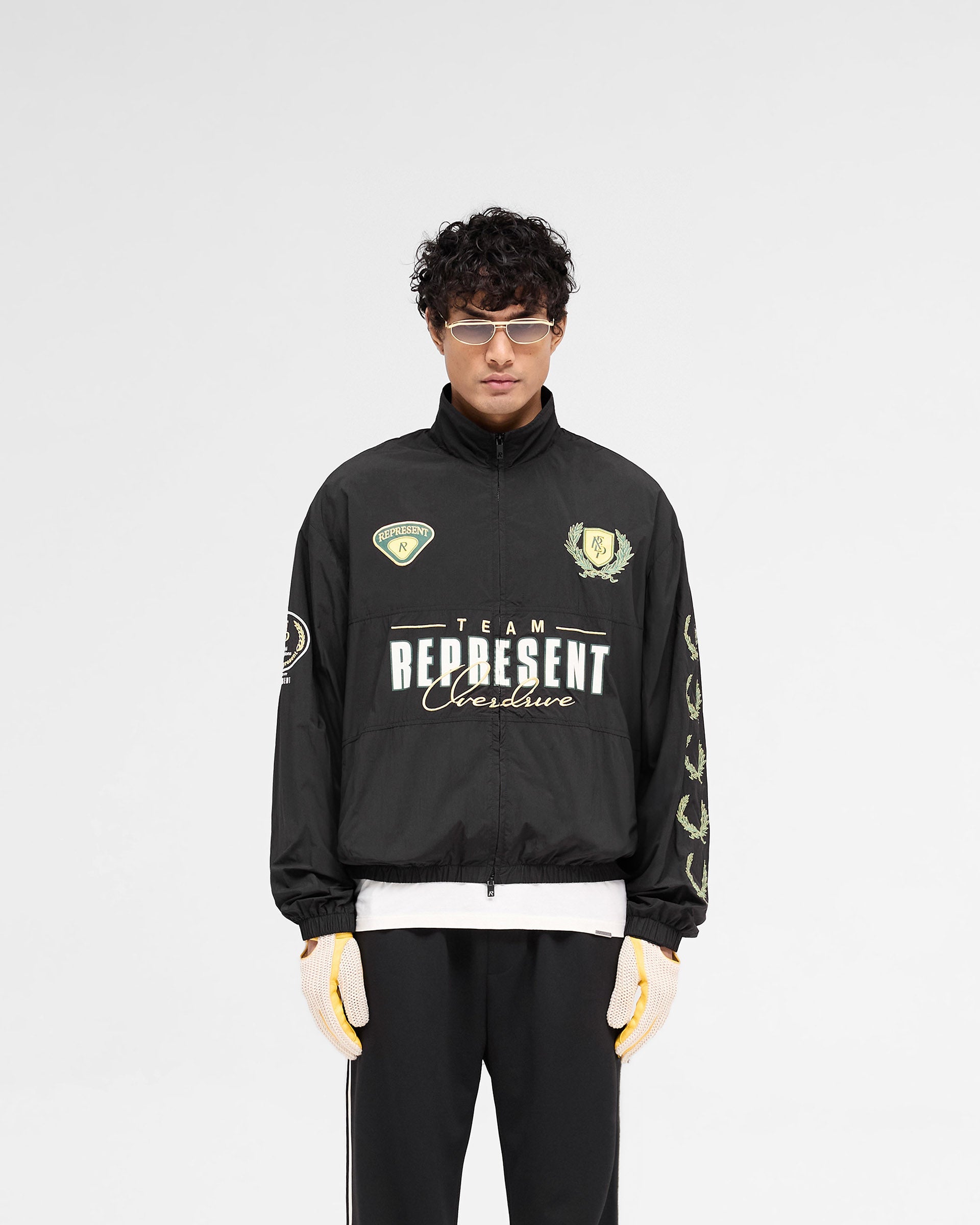 Man wearing a black track jacket on a plain white background | World Championship Track Jacket in Black | Lightweight track jacket with funnel neck and mesh lining | SS25 Outerwear | Represent Clo