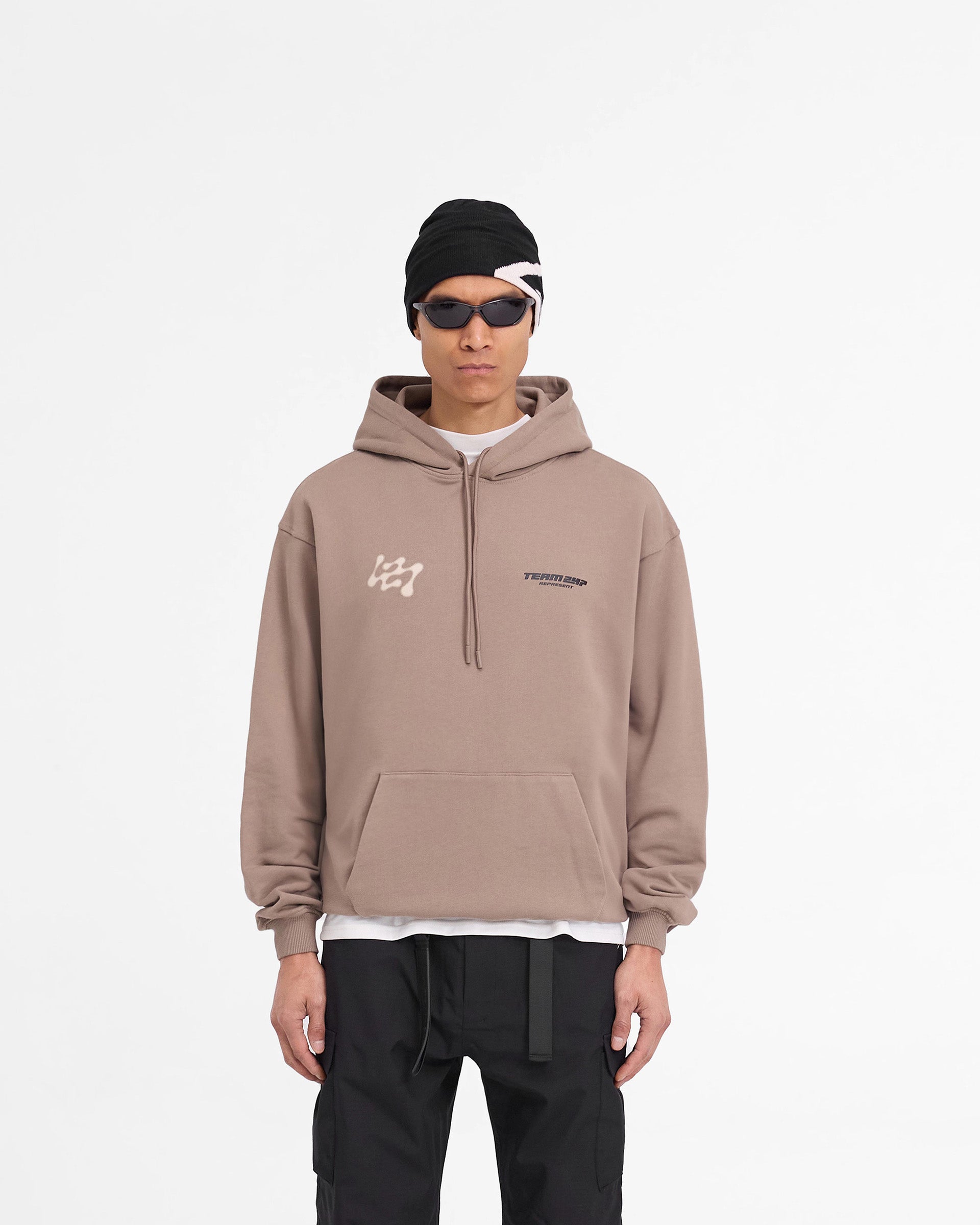 Man wearing an oversized brown hoodie on a plain white background | 247 Future Terrains Oversized Hoodie in Umber | Heavyweight hoodie with Team 247 branding and ribbed hem | 247 Hoodies | Represent Clo