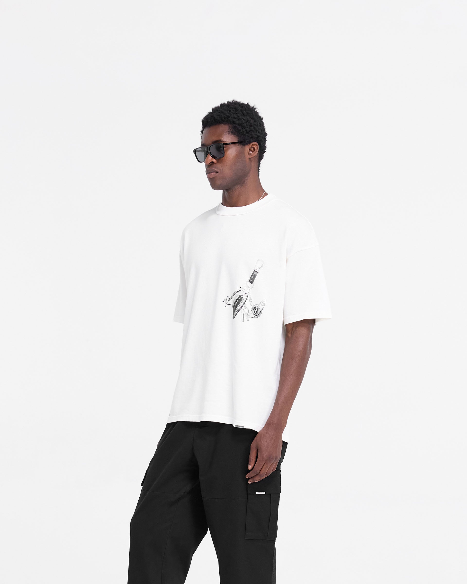 Man wearing a white t-shirt on a plain white background | Keys To The Club T-Shirt in Flat White | Slightly oversized t-shirt with graphic print | FW24 T-Shirts | Represent Clo