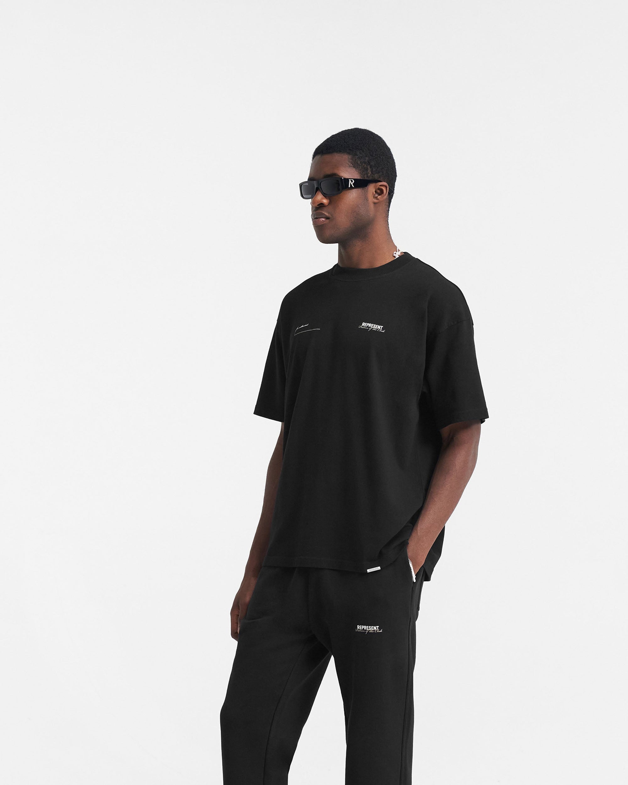 Man wearing a black oversized t-shirt on a plain white background | Patron Of The Club T-Shirt in Black | Oversized t-shirt with crewneck in medium weight cotton | Patrons T-Shirts | Represent Clo