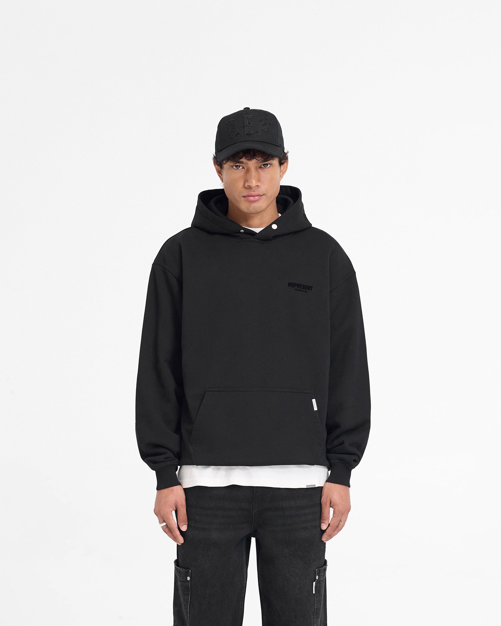 Man wearing a black hoodie on a plain white background | Represent Owners Club Flocked Hoodie in Black | Oversized hoodie with flocked print and ribbed trims | Owners Club Hoodies | Represent Clo