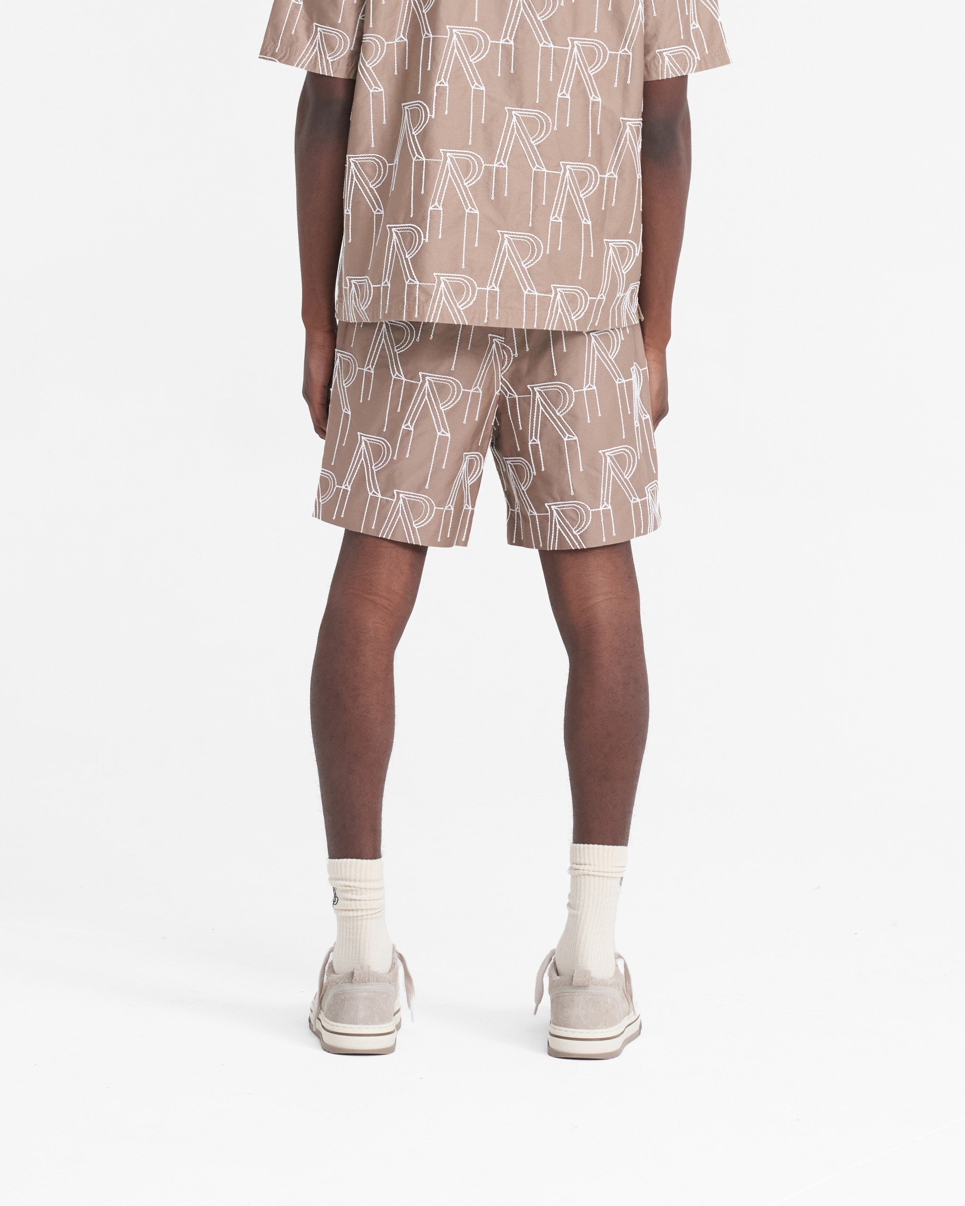 Man wearing washed taupe tailored shorts on a plain white background | Embroidered Initial Tailored Short in Washed Taupe | Shorts with raised chain stitch embroidery | SS24 Shorts | Represent Clo