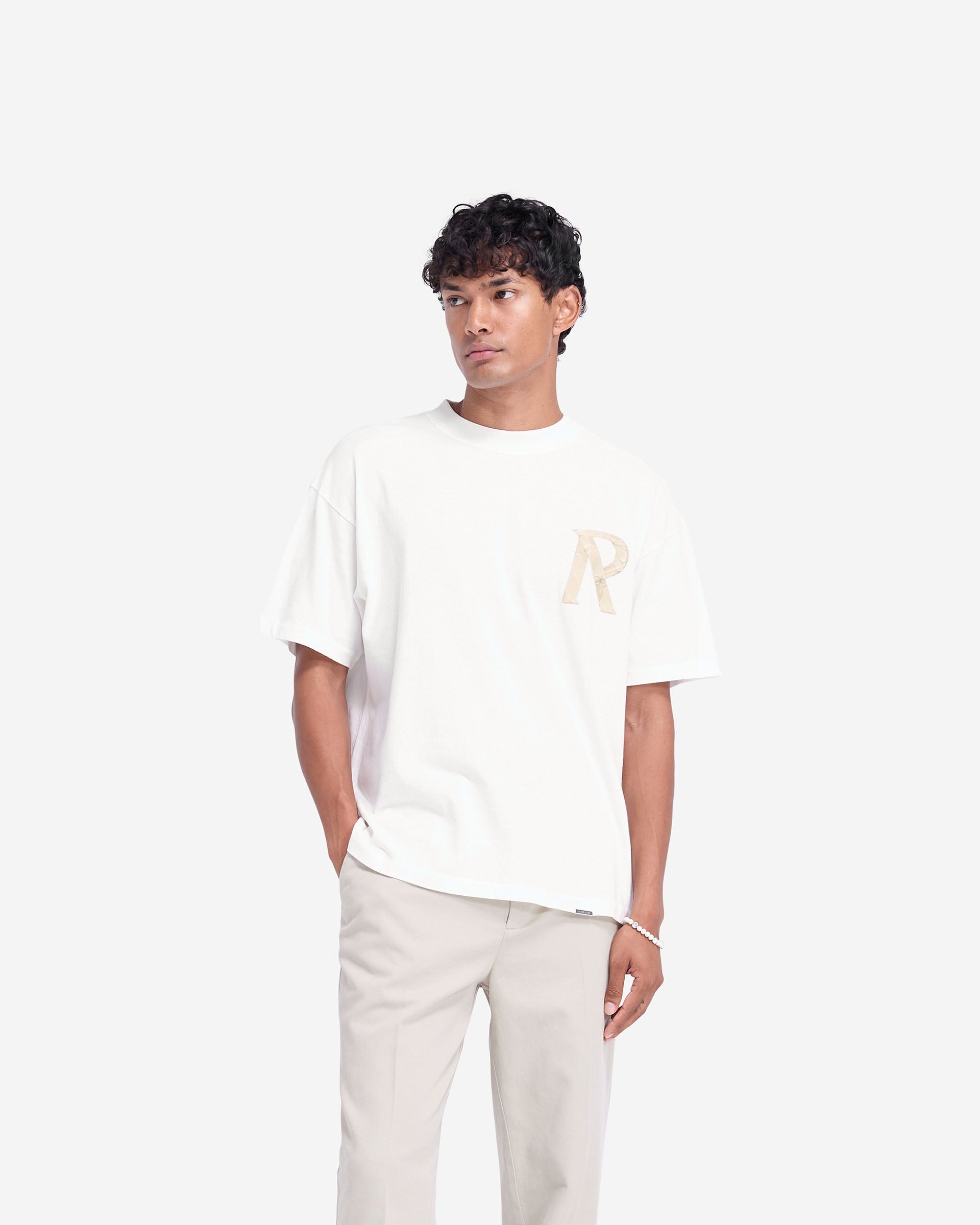 Man wearing a white t-shirt on a plain white background | Masking Tape Initial T-Shirt in Flat White | Oversized t-shirt with 3D masking tape effect initial | FW24 T-Shirts | Represent Clo