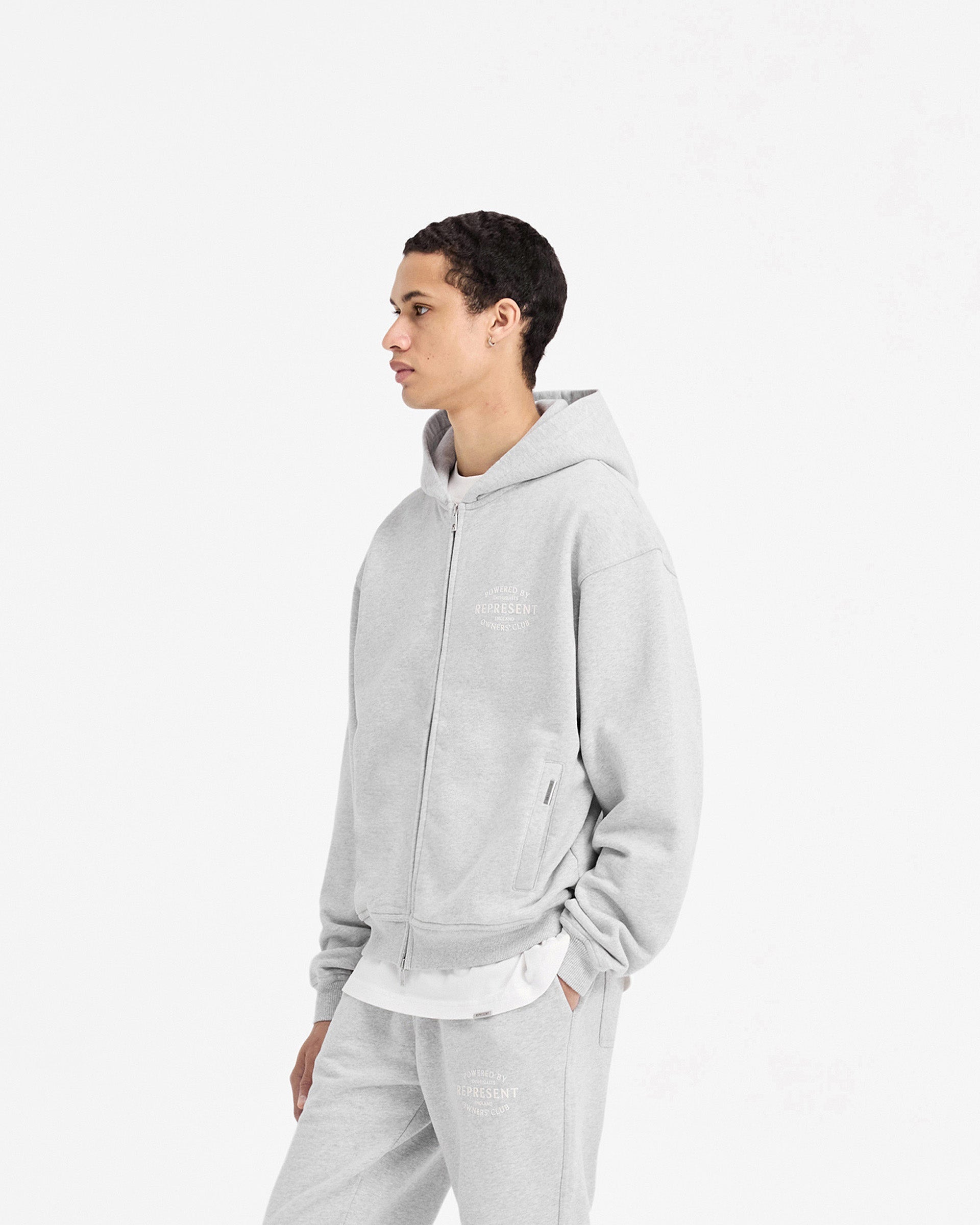 Man wearing a grey zip-up hoodie on a plain white background | Represent Owners Club Stamp Zip Up Hoodie in Ash Grey | Hoodie with slightly oversized fit and high build branding | Owners Club Hoodies | Represent Clo
