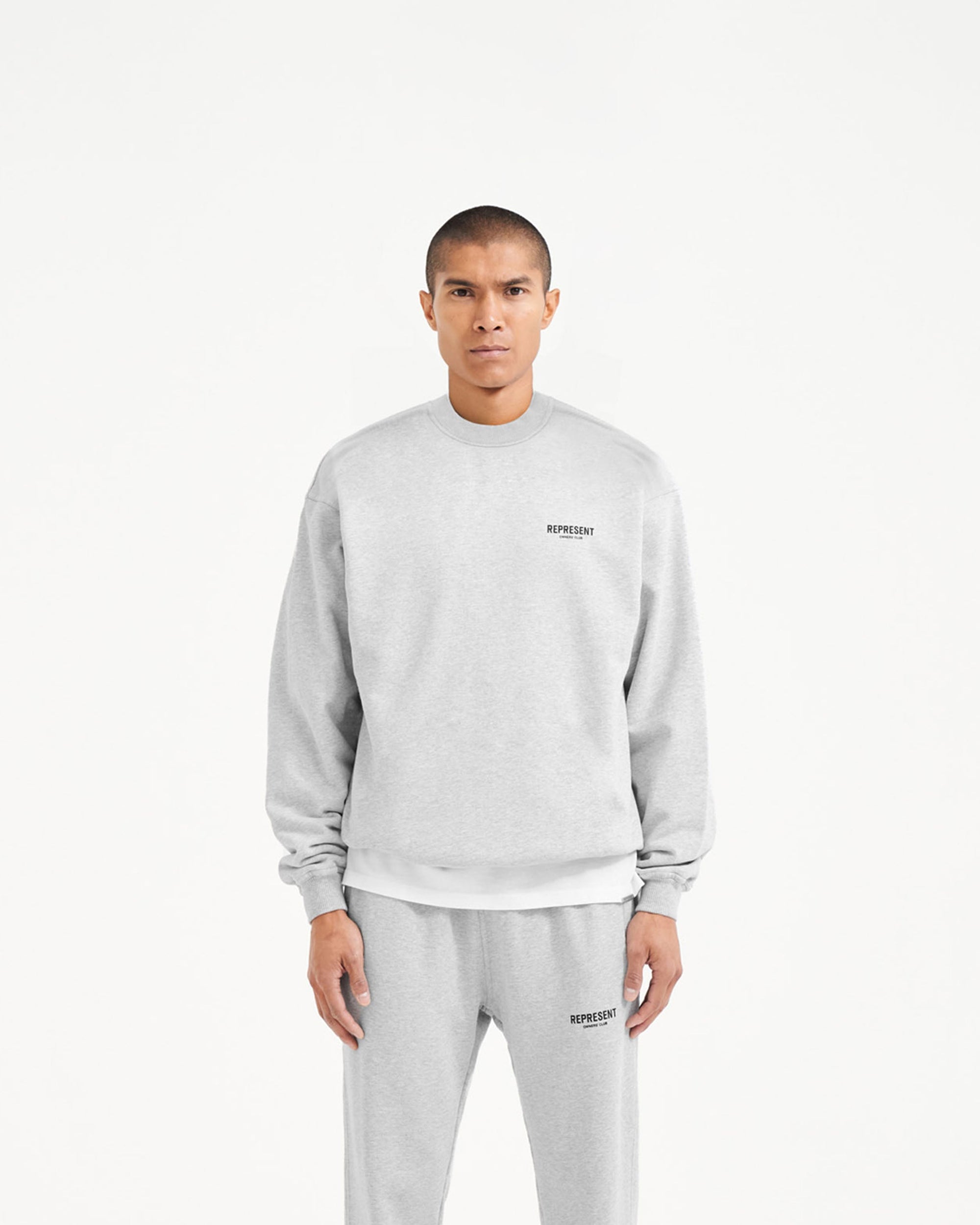 Man wearing an oversized grey sweater on a plain white background | Represent Owners Club Sweater in Ash Grey | Crewneck sweater with Owners Club branding | Owners Club Sweaters | Represent Clo