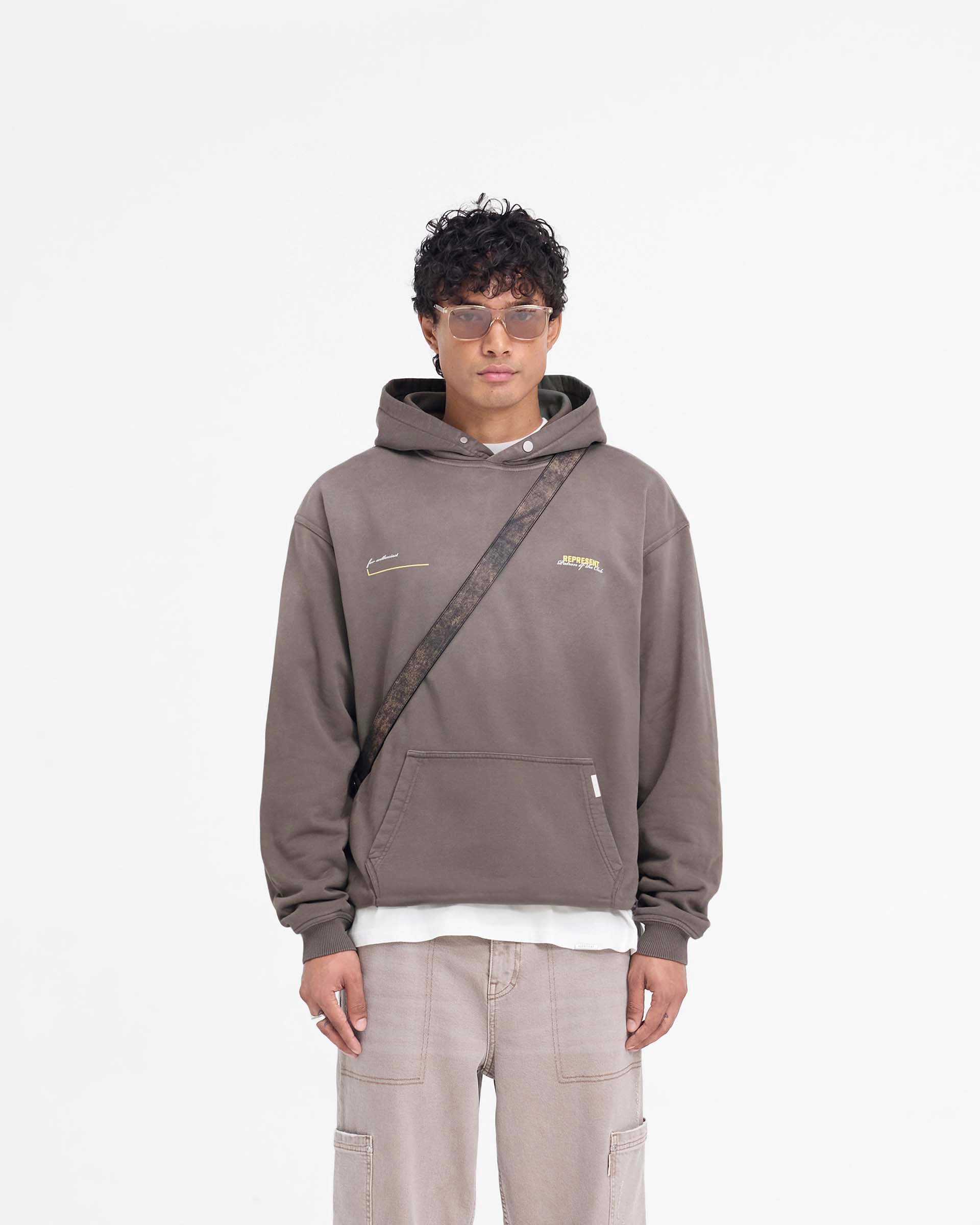 Man wearing an oversized olive hoodie on a plain white background | Patron Of The Club Hoodie in Washed Olive | Oversized hoodie with Patron of the Club print | Patrons Hoodies | Represent Clo