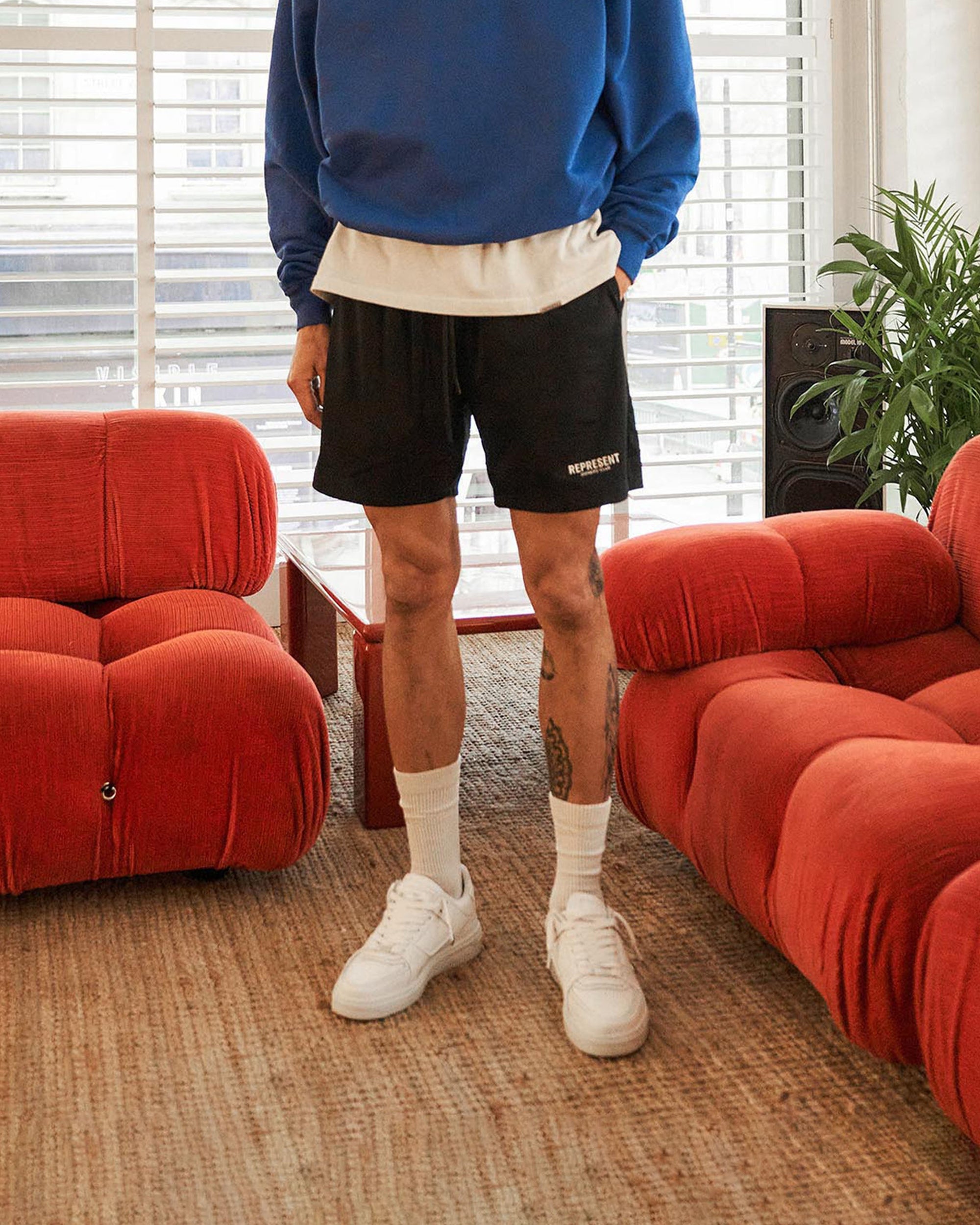 Man wearing black mesh shorts on a plain white background | Represent Owners Club Mesh Shorts in Black | Relaxed fit mesh shorts with elasticated waist | Owners Club Shorts | Represent Clo