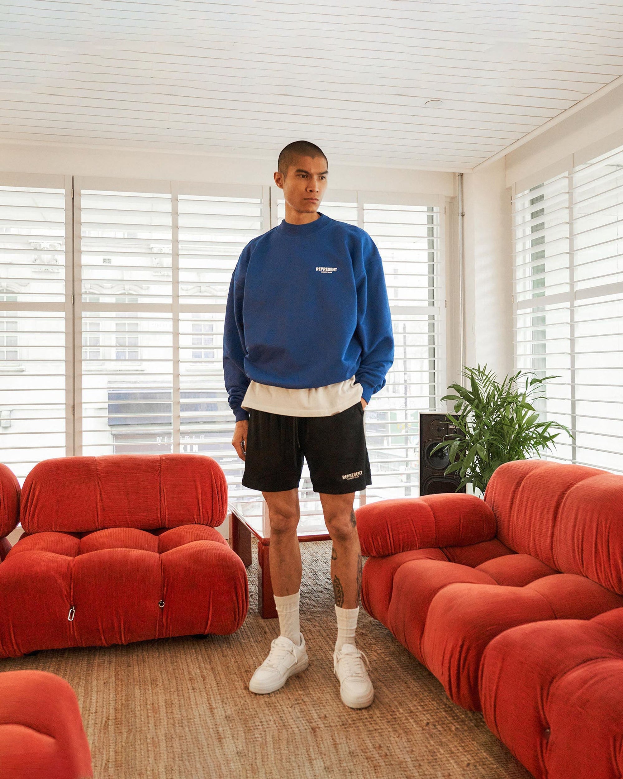 Man wearing black mesh shorts on a plain white background | Represent Owners Club Mesh Shorts in Black | Relaxed fit mesh shorts with elasticated waist and welt pockets | Owners Club Shorts | Represent Clo