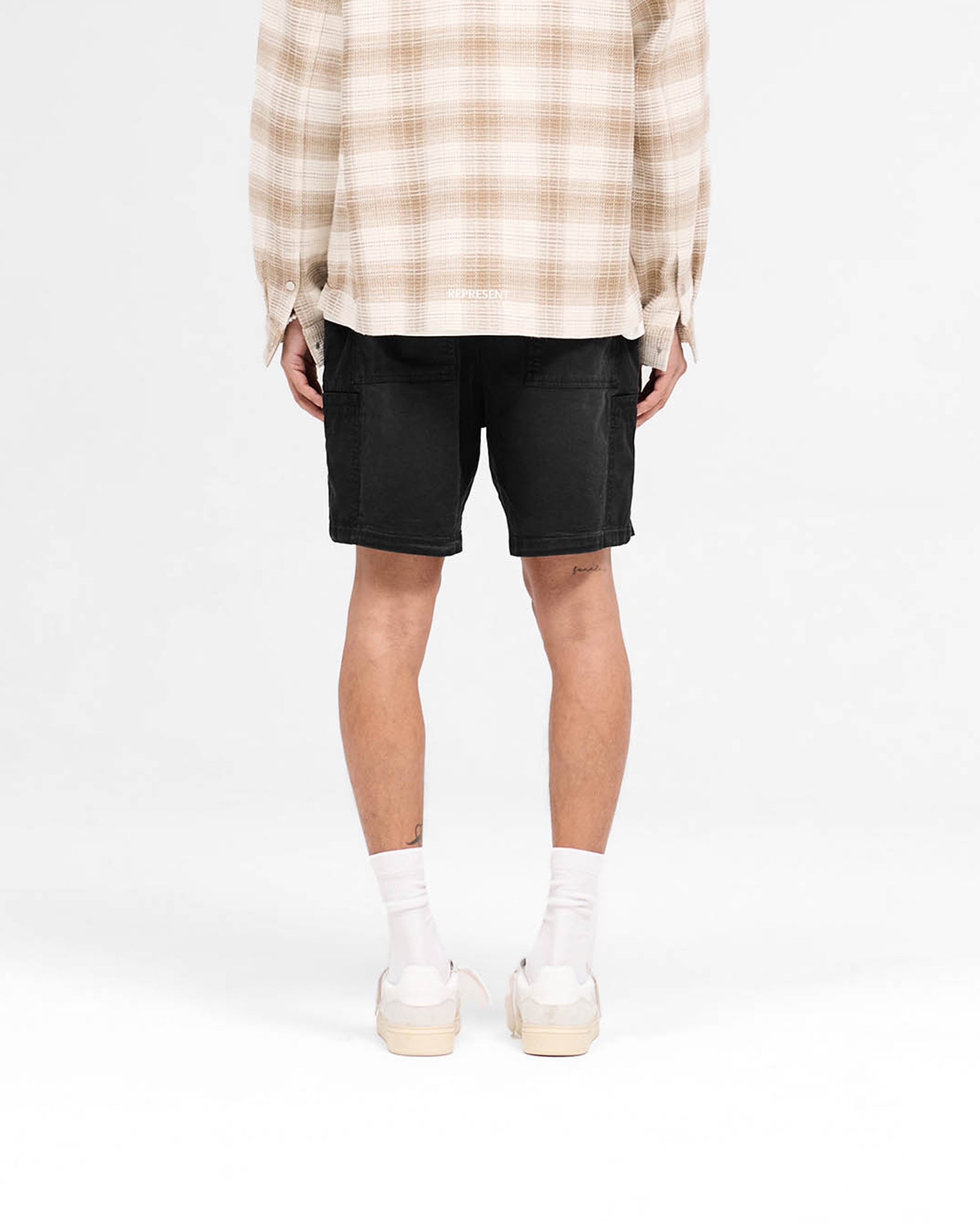 Man wearing black cargo shorts on a plain white background | Season Cargo Short in Jet Black | Brushed twill shorts with welt cargo pockets | SS25 Shorts | Represent Clo