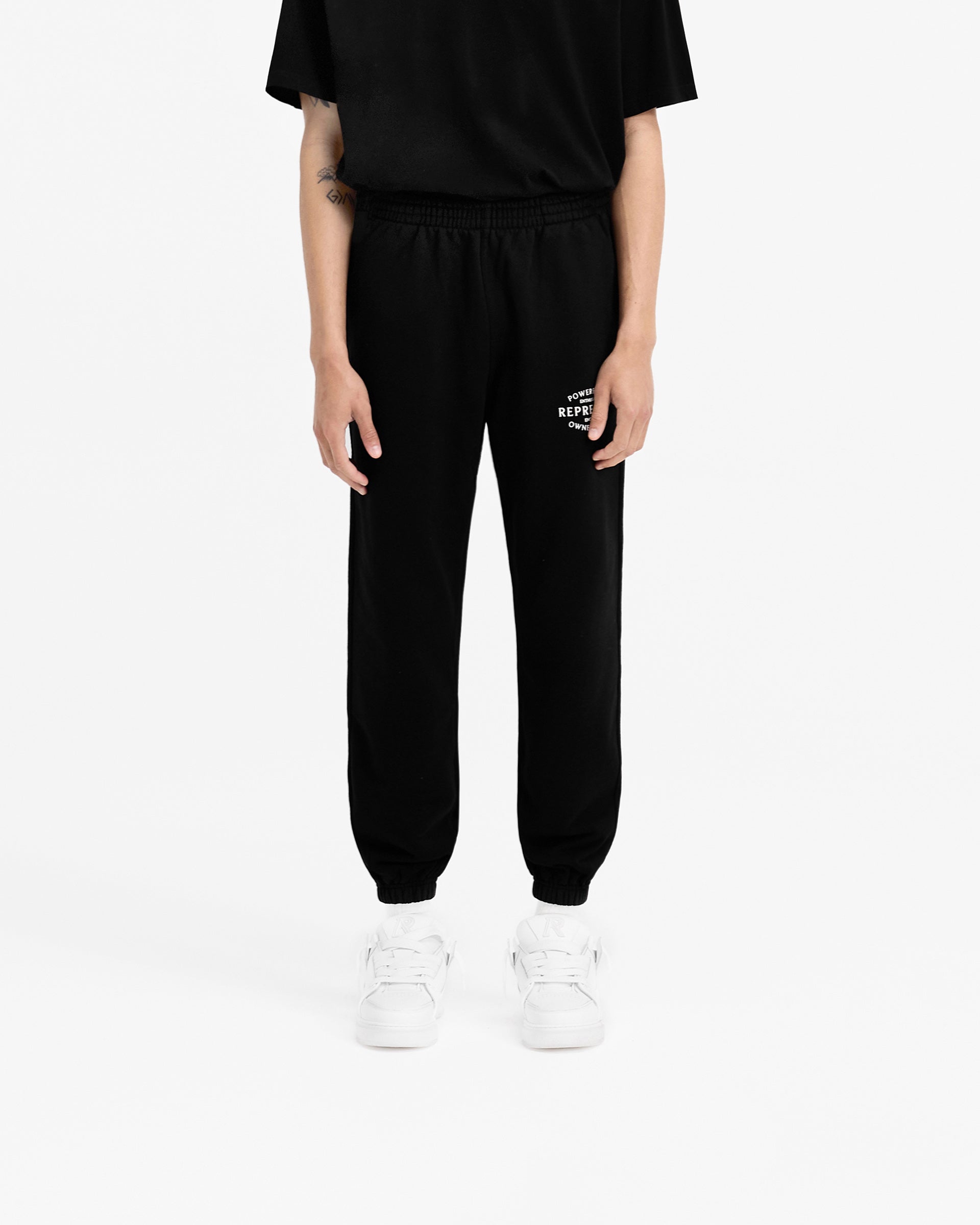 Man wearing black sweatpants on a plain white background | Owners Club Stamp Sweatpant in Jet Black | Sweatpants with elasticated waistband and cuffs | Owners Club Pants | Represent Clo