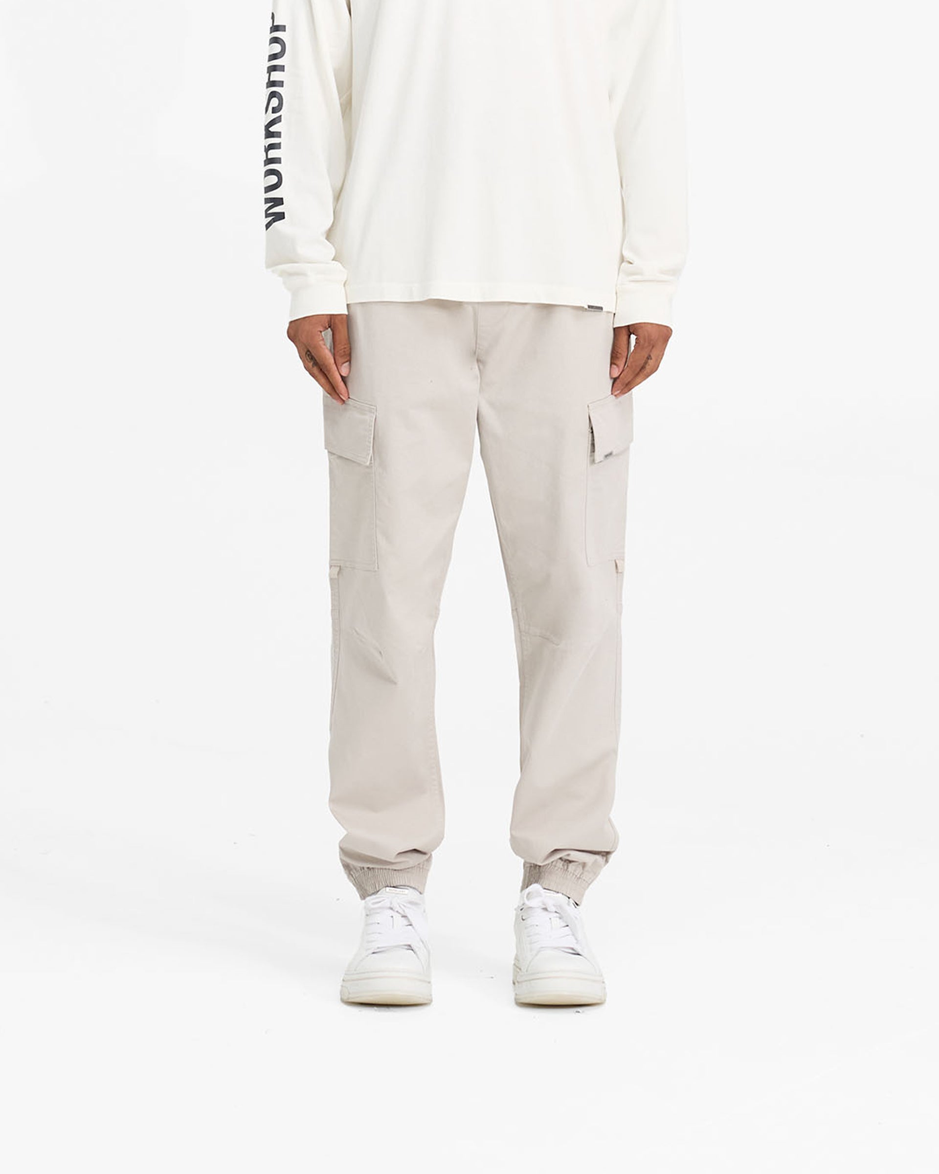 Man wearing stone cargo pants on a plain white background | Cuffed Cargo Pant in Stone | Cargo pants with elasticated waistband and cuffs | FW24 Pants | Represent Clo