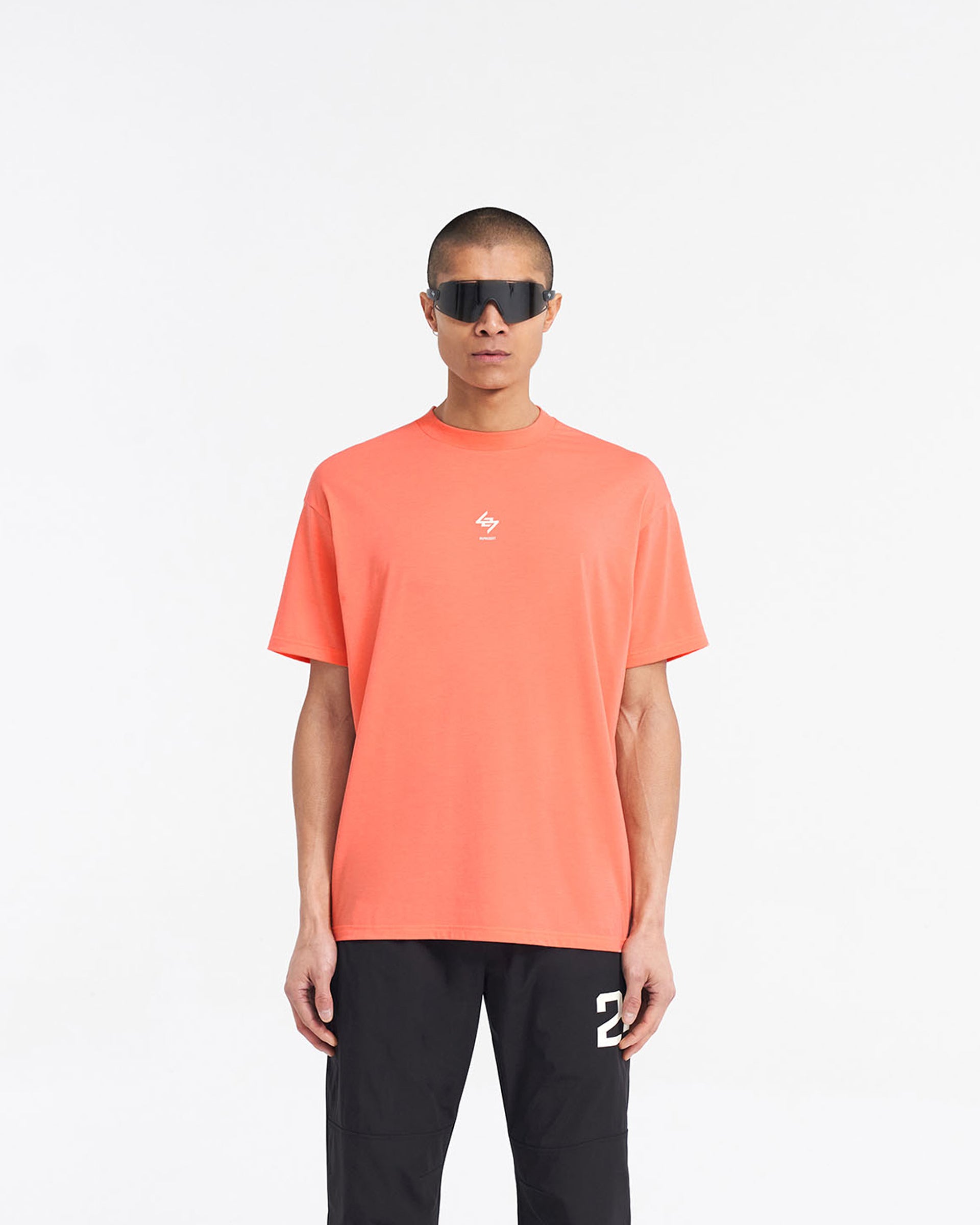 Man wearing an oversized coral t-shirt on a plain white background | 247 Oversized T-Shirt in Coral | Lightweight gym t-shirt with 4-way stretch | 247 T-Shirts | Represent Clo