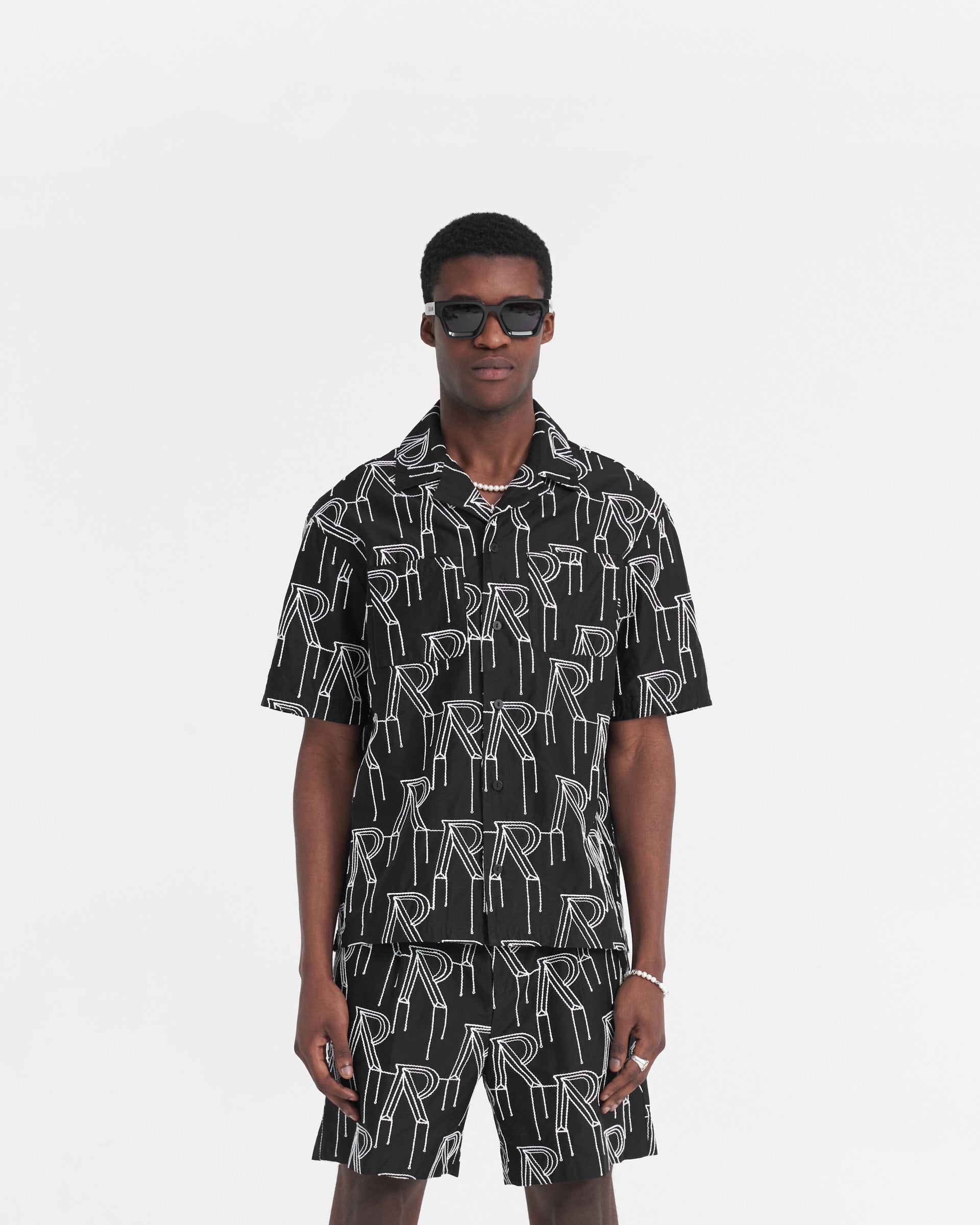 Man wearing a black short-sleeved shirt on a plain white background | Embroidered Initial Overshirt in Black | Oversized shirt with chain stitch embroidery | SS24 Shirts | Represent Clo
