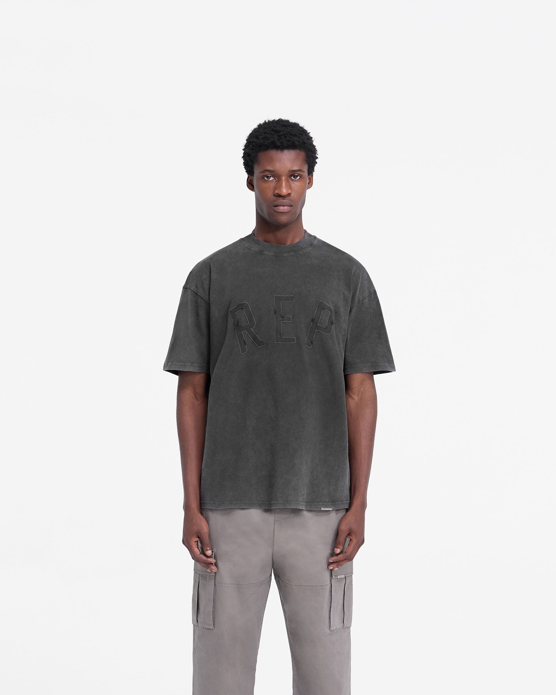 Man wearing a black t-shirt on a plain white background | Rep Applique T-Shirt in Vintage Black | Oversized t-shirt with distressed applique logo | FW24 T-Shirts | Represent Clo