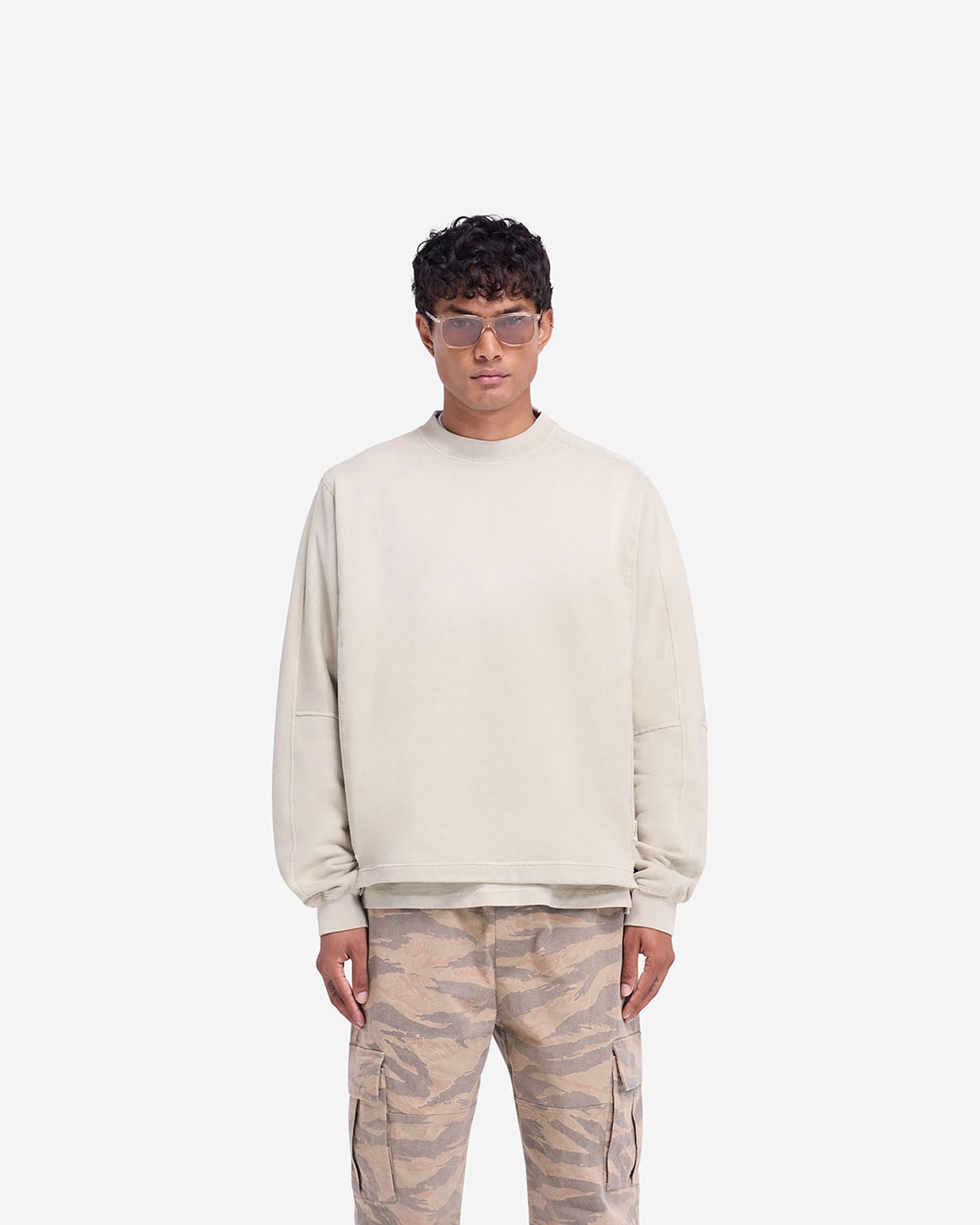 Man wearing an oversized oat sweatshirt on a plain white background | Stepped Hem Sweatshirt in Oat | Oversized sweater with stepped hem and sun fade wash | FW24 Sweaters | Represent Clo
