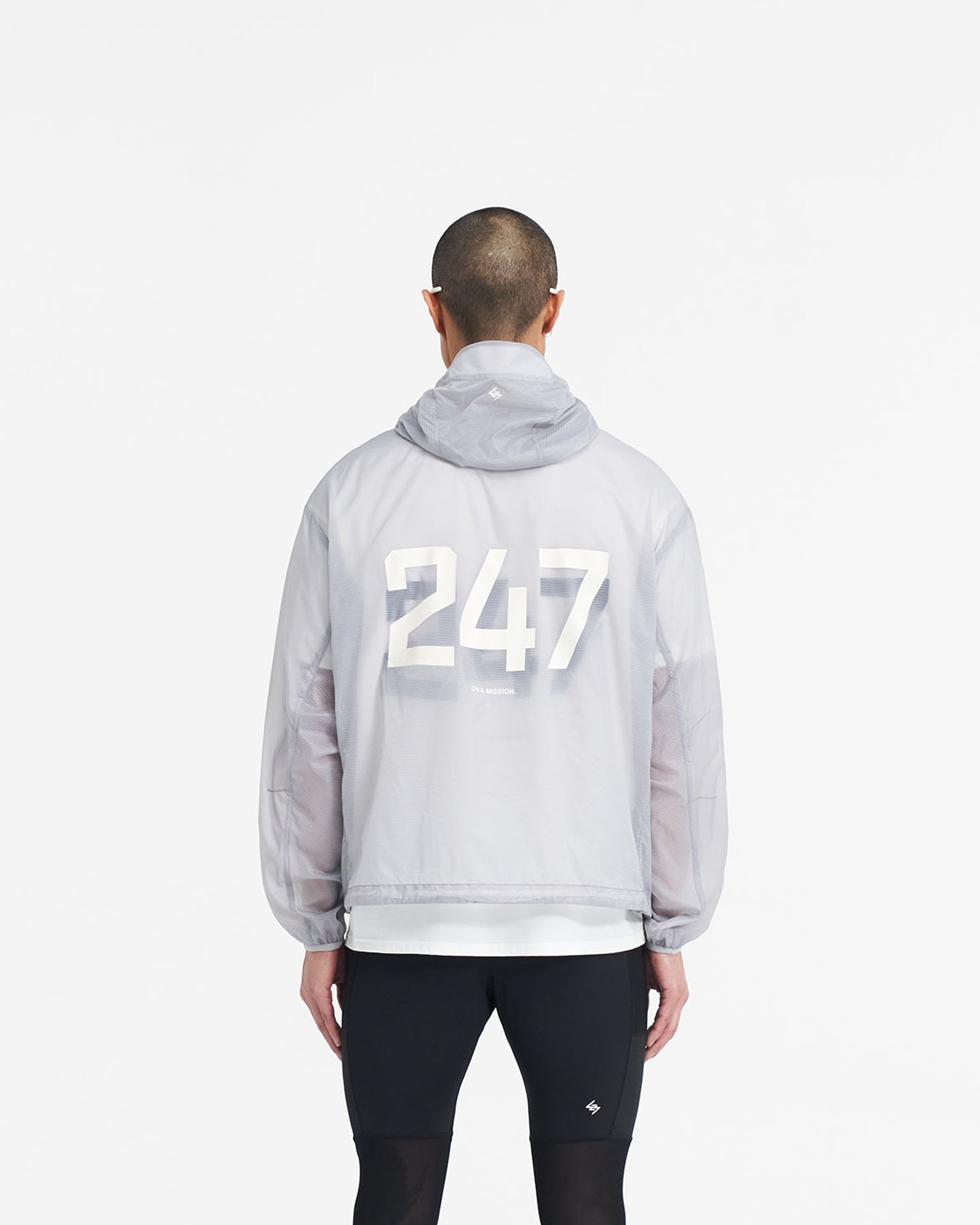 Man wearing a translucent grey hooded jacket on a plain white background | 247 Hooded Training Jacket in Moonstone | Nylon ripstop outerwear with adjustable hem | 247 Outerwear | Represent Clo