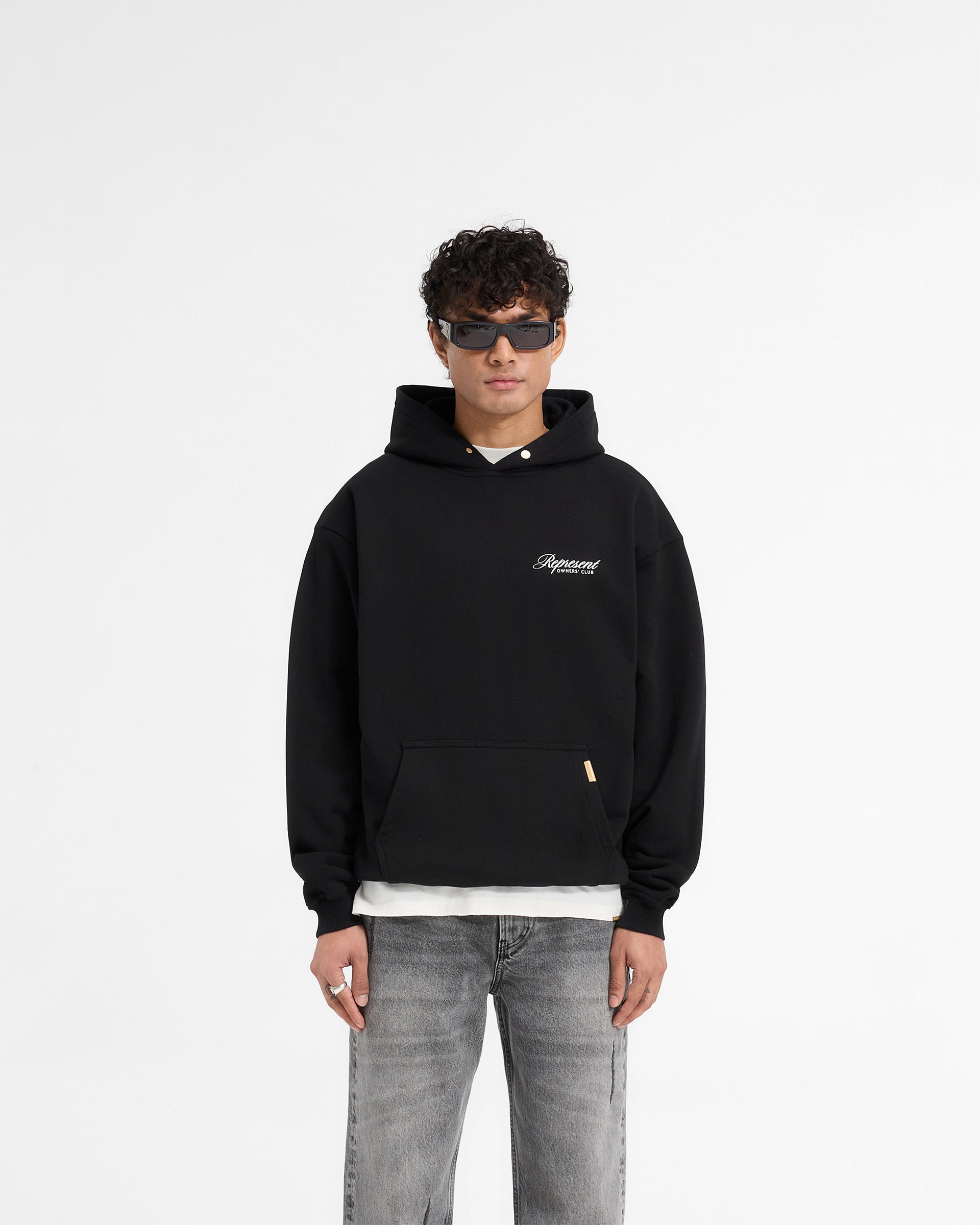 Man wearing a black hoodie on a plain white background | Represent X Harrods Bear Owners Club Hoodie in Jet Black | Oversized hoodie with Harrods bear graphic | Exclusives Hoodies | Represent Clo