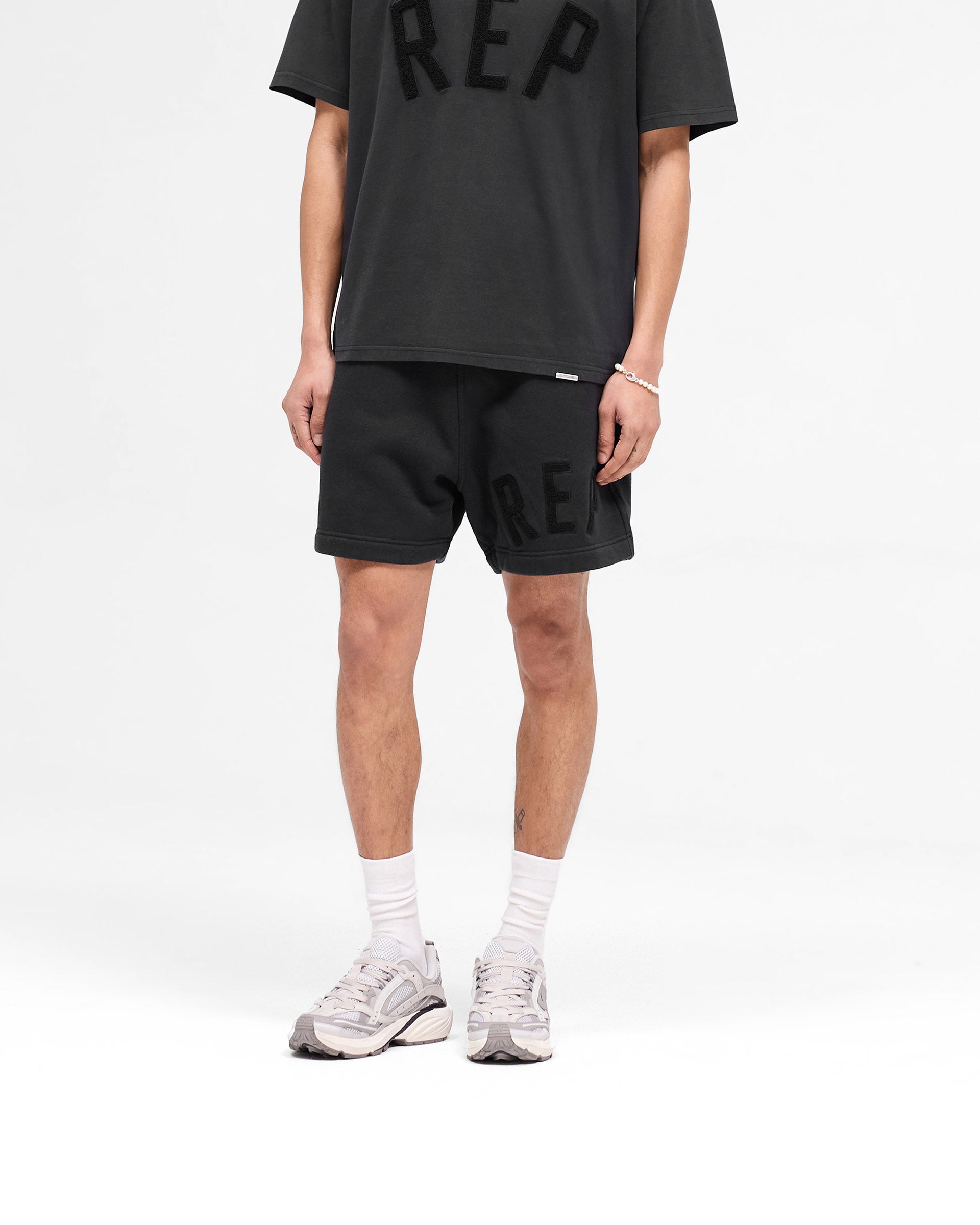 Back product image of mens black shorts on a plain white background | Rep Applique Shorts in Off Black | Shorts with elasticated waistband and back pockets | SS25 Shorts | Represent Clo