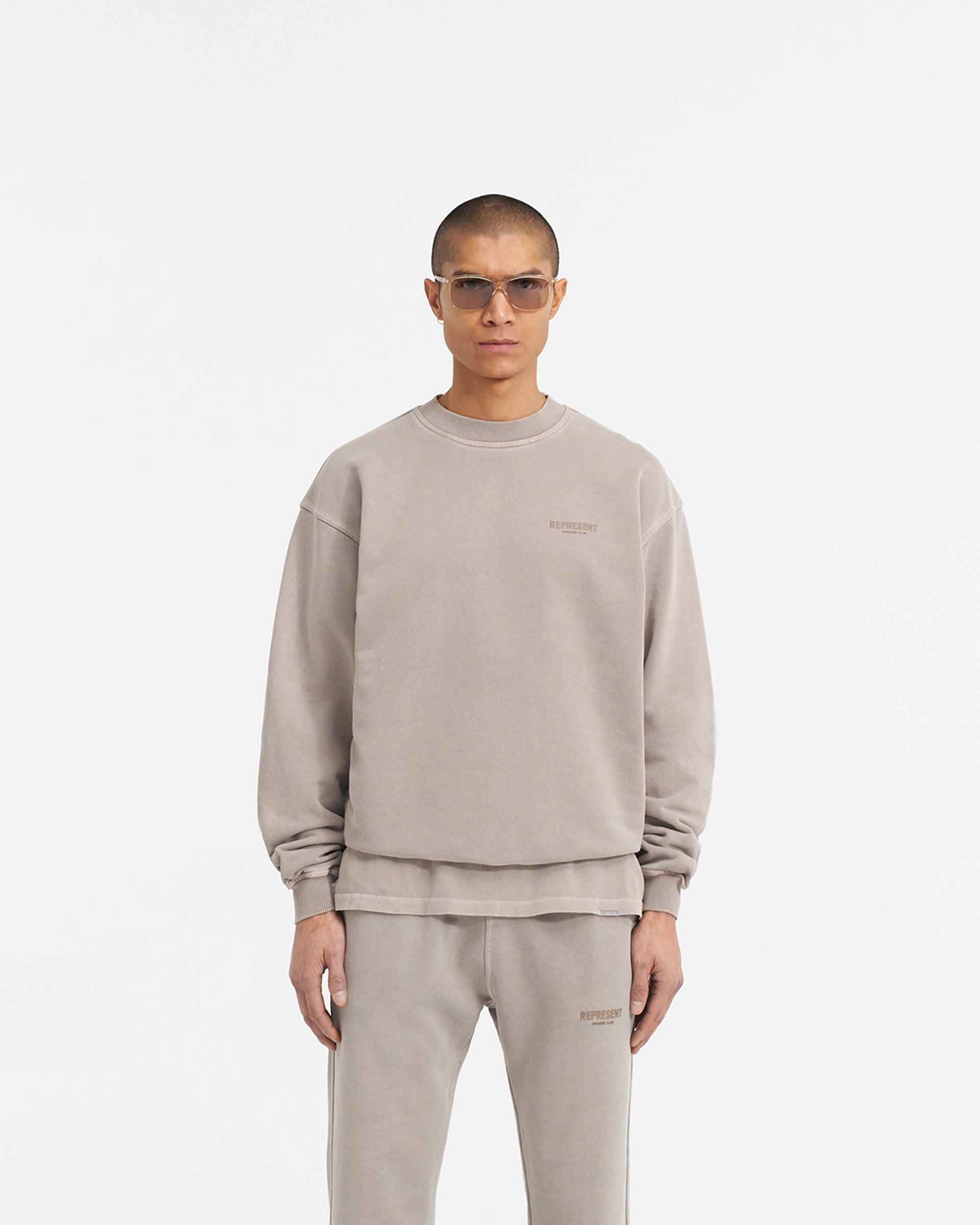 Man wearing a beige sweater on a plain white background | Represent Owners Club Sweater in Mushroom | Oversized crewneck sweater with ribbed trims | Owners Club Sweaters | Represent Clo