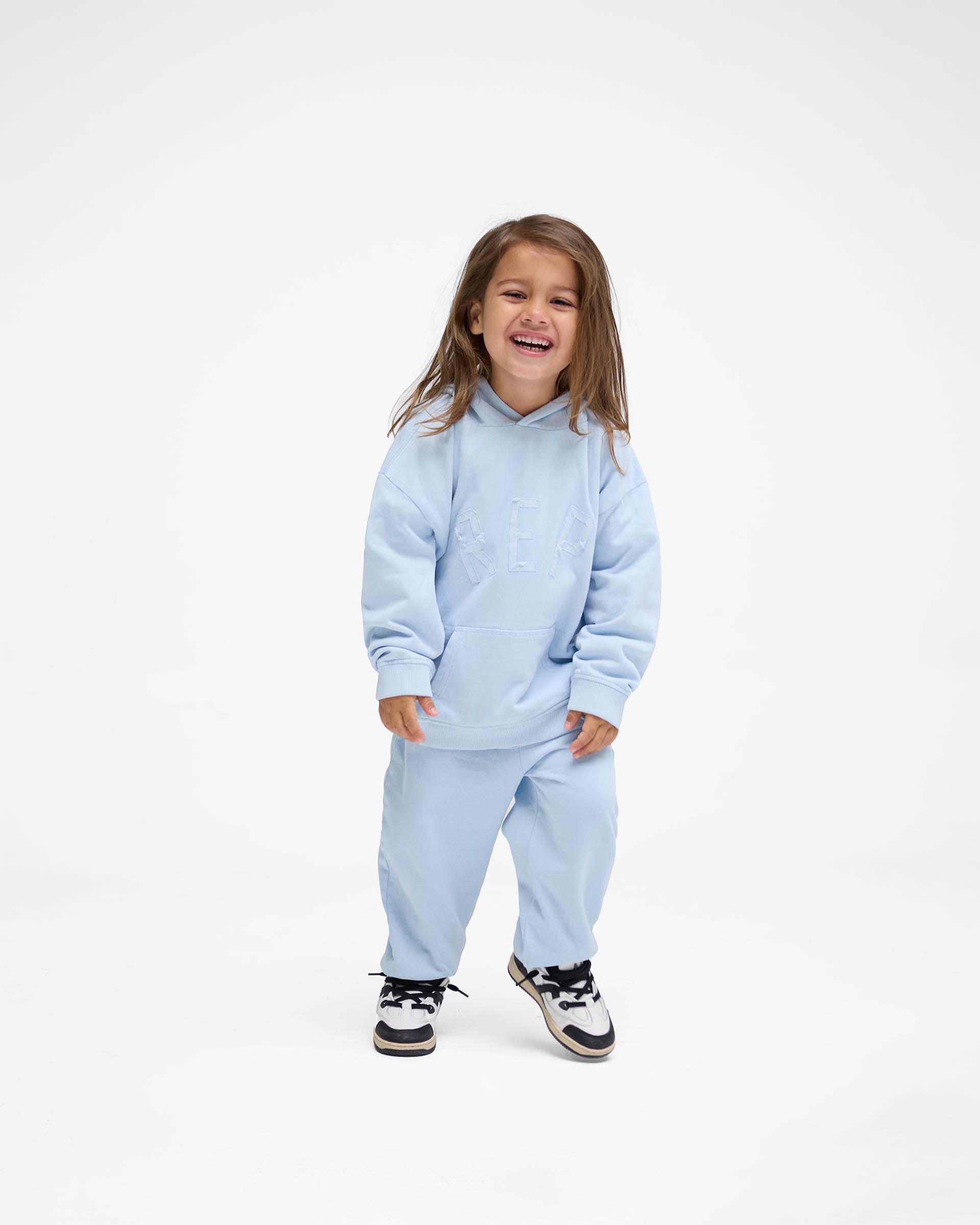 Back product image of a kids blue hoodie on a plain white background | Mini Rep Applique Hoodie in Powder Blue | Kids hoodie with overlock stitching and distressed applique logo | FW24 Hoodies | Represent Clo