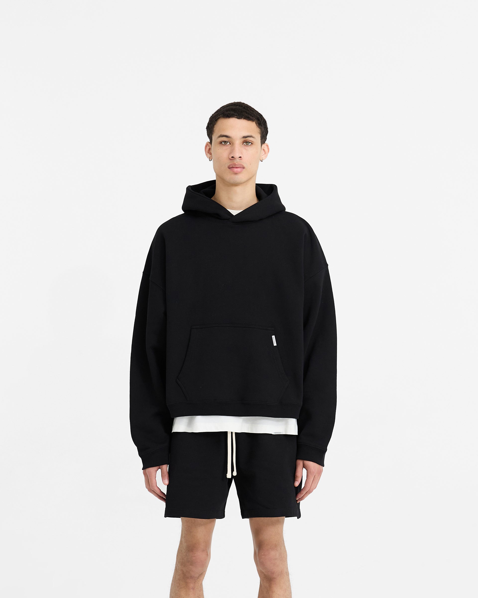 Man wearing a boxy black hoodie on a plain white background | Initial Boxy Hoodie in Black | Oversized cropped hoodie with dropped shoulders | Initial Hoodies | Represent Clo
