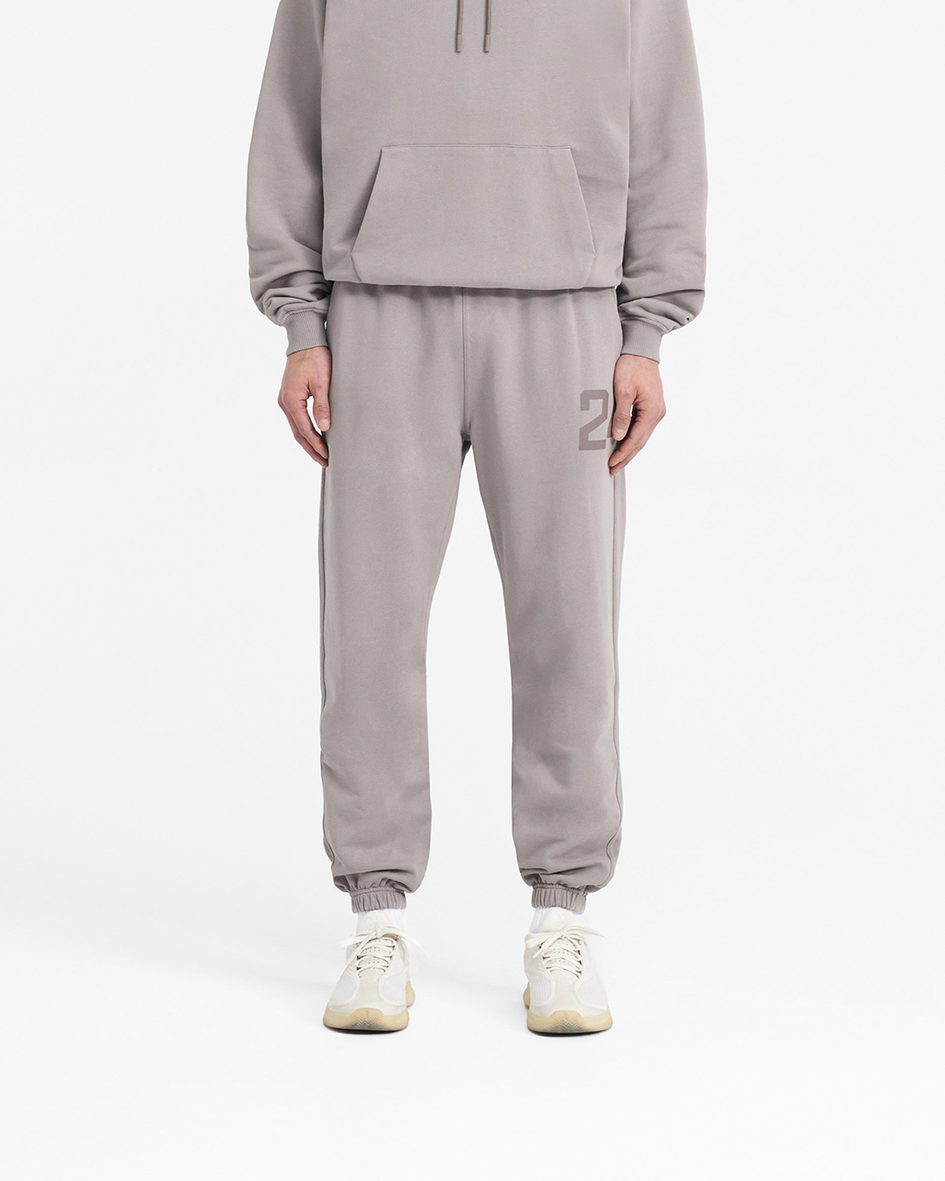 Man wearing grey sweatpants on a plain white background | 247 Sweatpant in Cinder | Joggers with elasticated cuffs & drawcord waistband | 247 Pants | Represent Clo