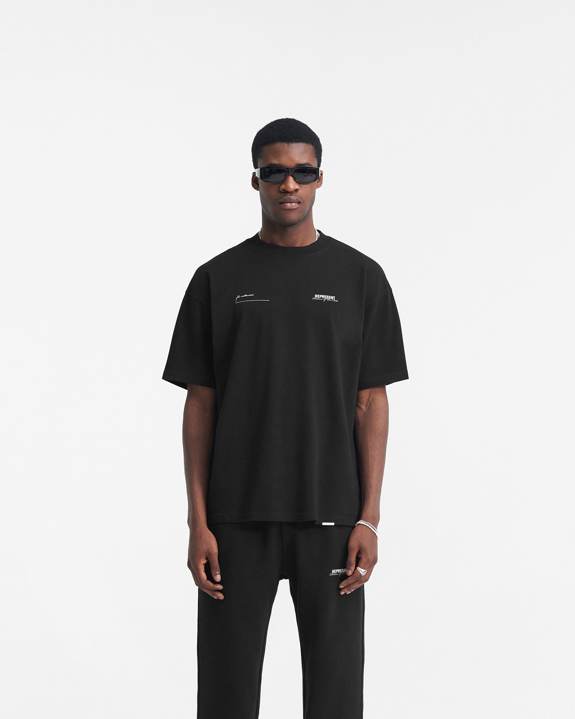 Man wearing a black t-shirt on a plain white background | Patron Of The Club T-Shirt in Black | Oversized t-shirt with ribbed crew neck and chest branding | Patrons T-Shirts | Represent Clo