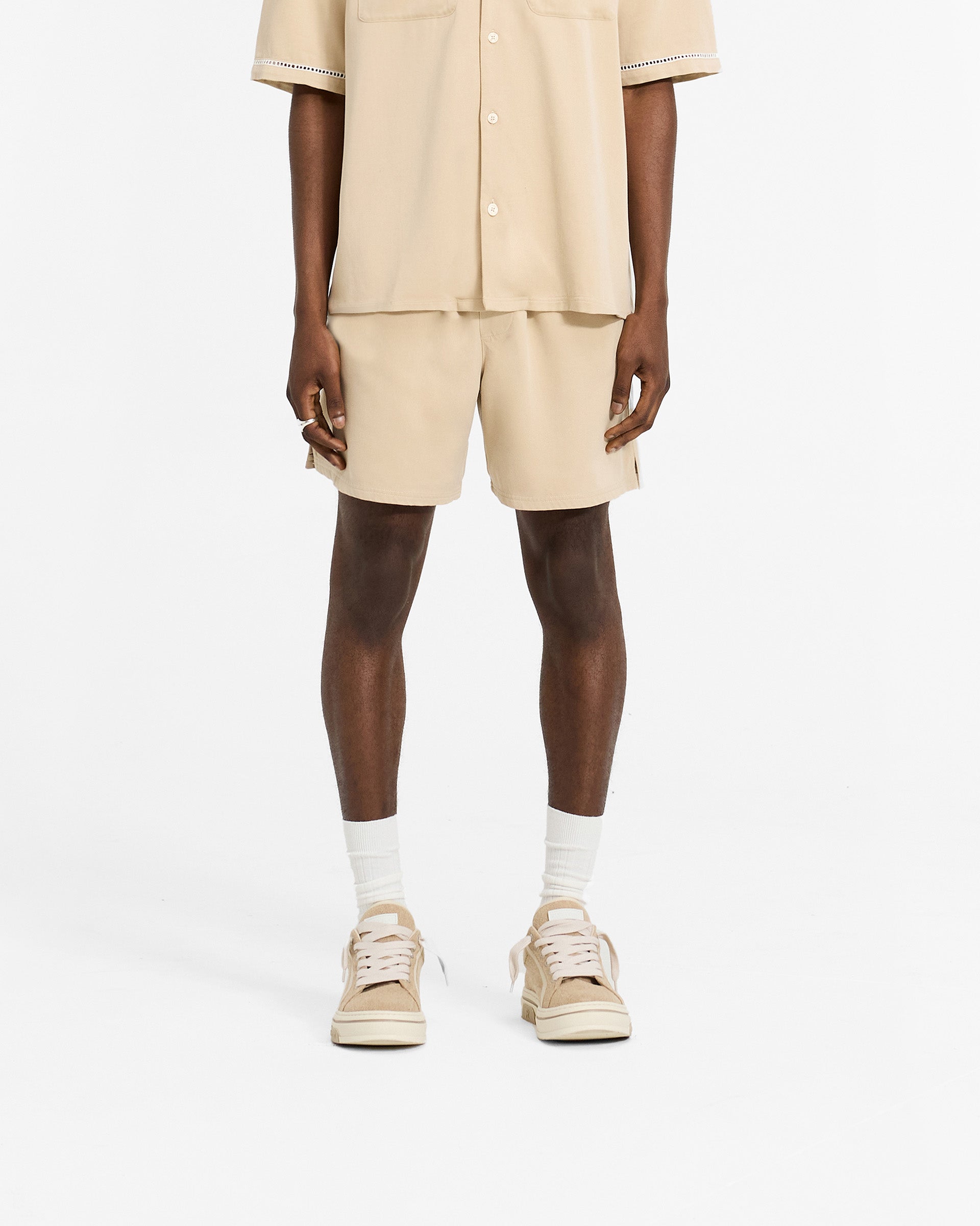 Man wearing latte brown relaxed fit shorts on a plain white background | Resort Shorts in Latte | Shorts with elasticated waistband and drawcord | SC24 Shorts | Represent Clo