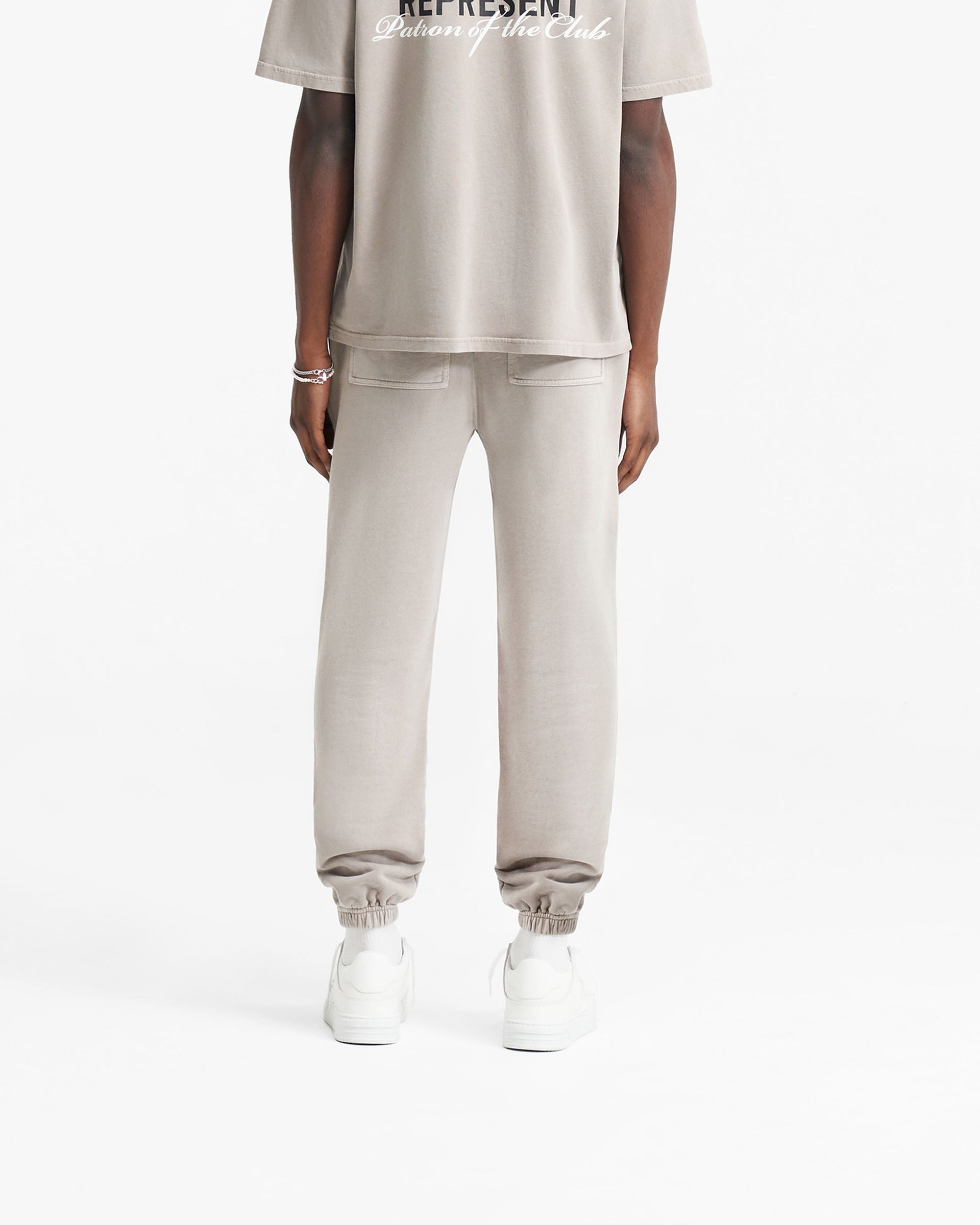 Man wearing mudstone sweatpants on a plain white background | Patron Of The Club Sweatpant in Mudstone | Sweatpants with elasticated waistband and cuffs | Patrons Pants | Represent Clo