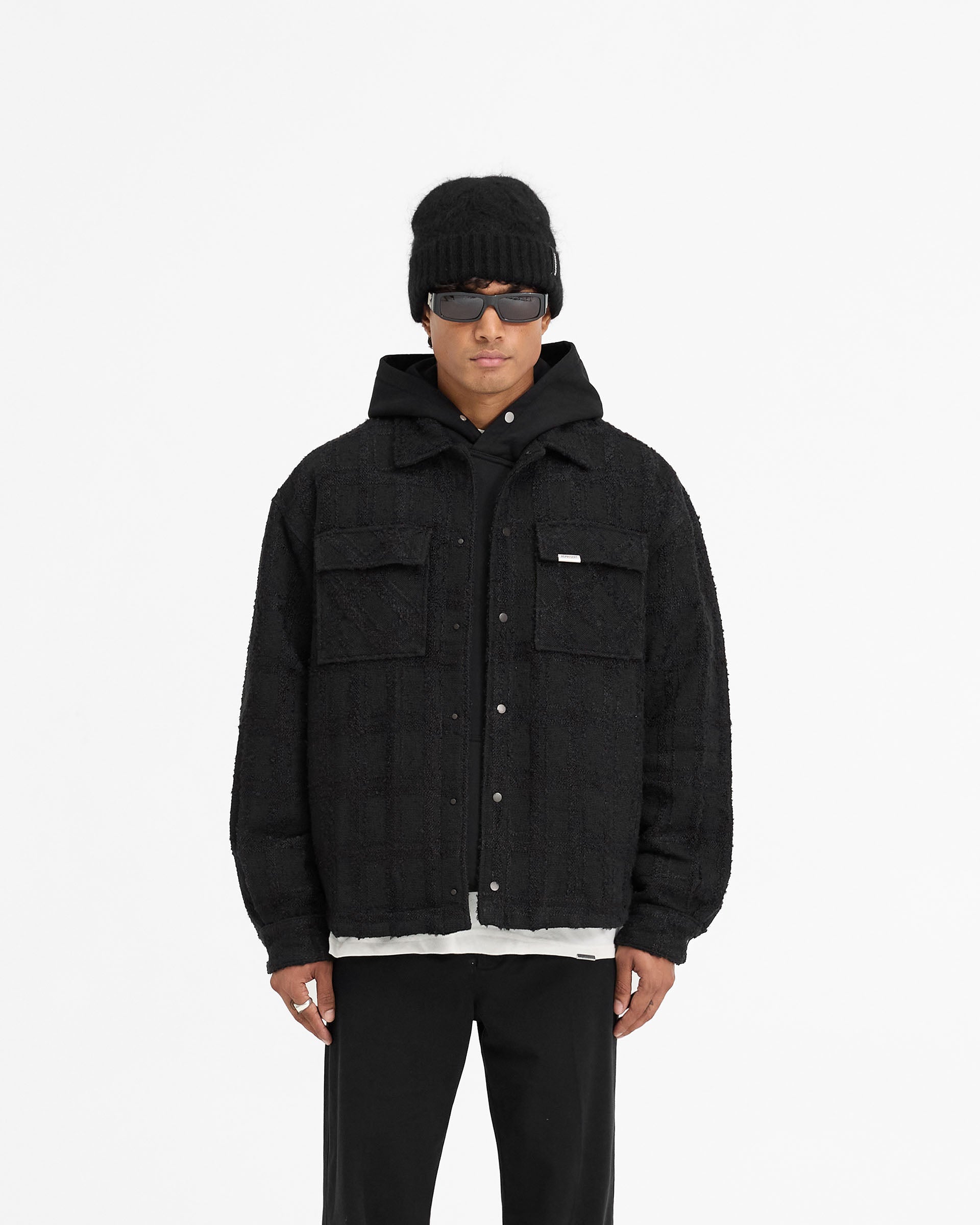 Man wearing a black overshirt on a plain white background | Wadded Overshirt in Black | Luxury overshirt with matte popper closures and flap pockets | FW24 Shirts | Represent Clo