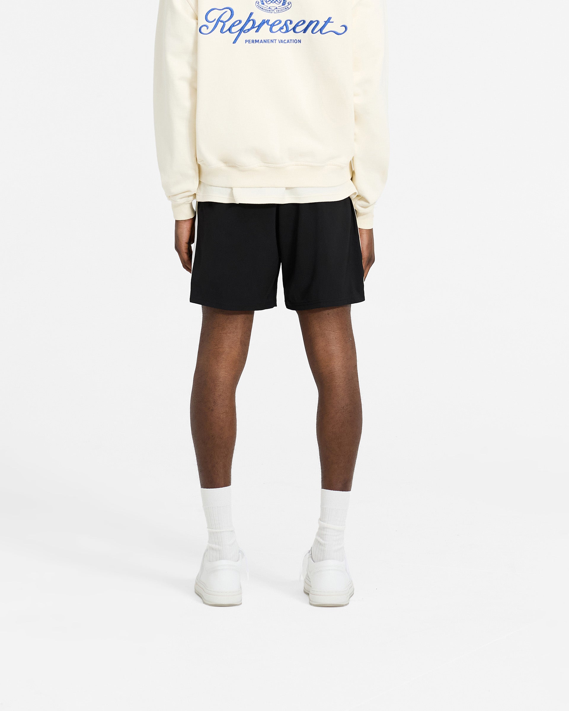 Man wearing relaxed fit black shorts with side stripes on a plain white background | Track Short in Jet Black | Shorts with elasticated waistband and side seam pockets | SC24 Shorts | Represent Clo