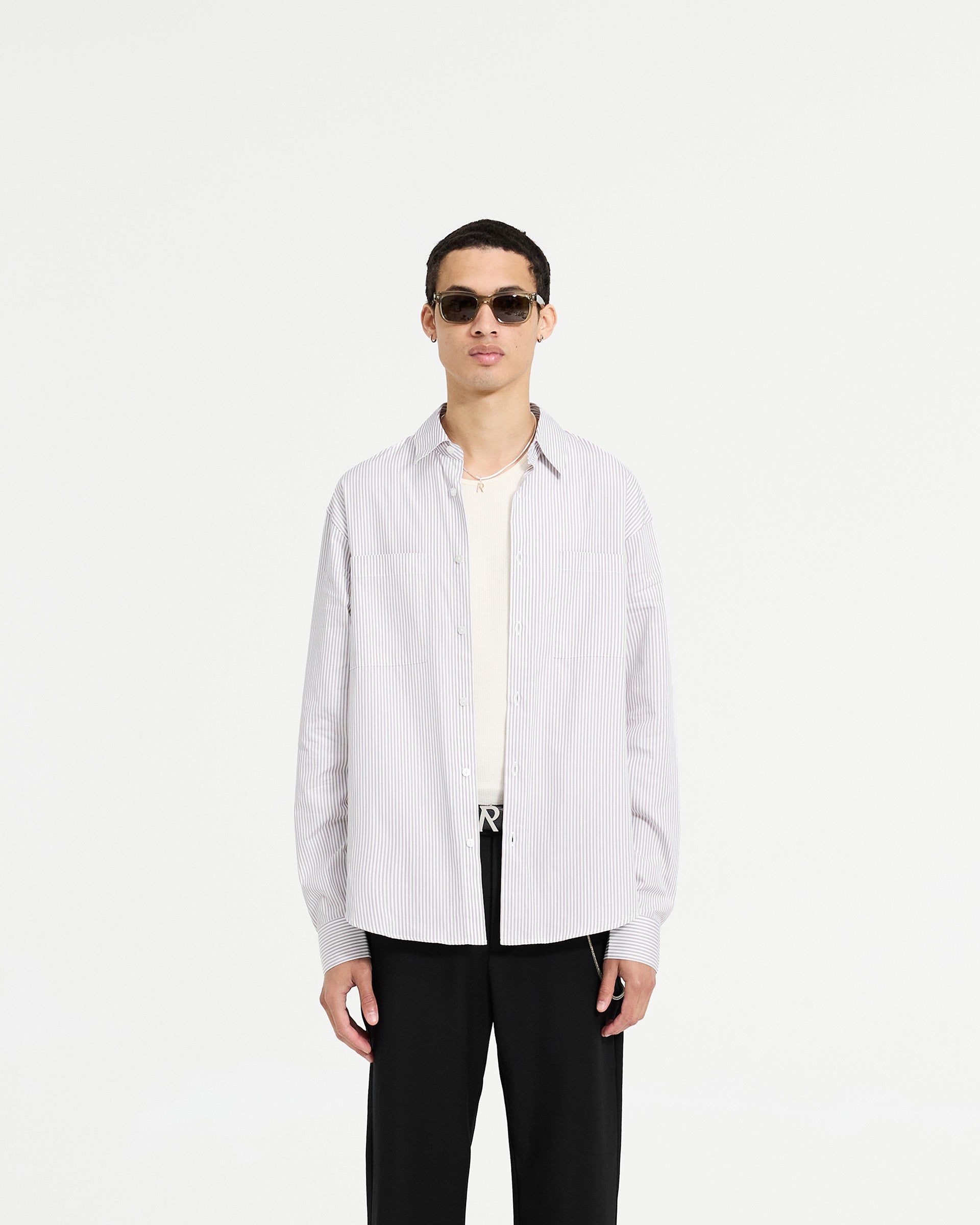 Man wearing a grey pinstripe long sleeve shirt on a plain white background | Long Sleeve Pinstripe Shirt in Grey | Oversized shirt with curved hem and chest pockets | SC24 Shirts | Represent Clo