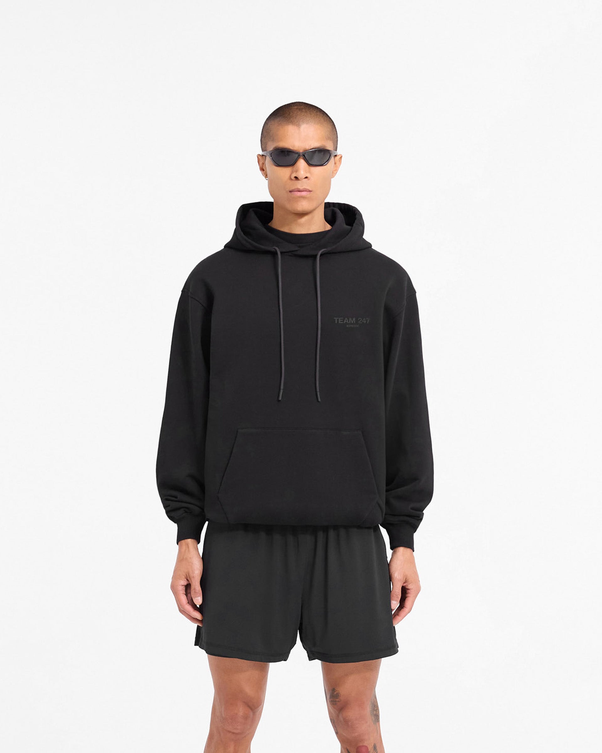 Man wearing an oversized black hoodie on a plain white background | Team 247 Oversized Hoodie in Matte Black | Oversized fit hoodie with matte black print | 247 Hoodies | Represent Clo