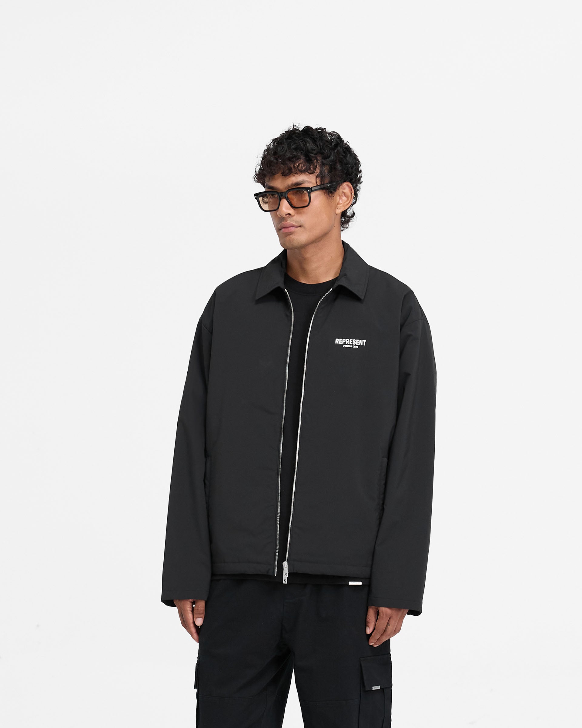 Man wearing a black coach jacket on a plain white background | Represent Owners Club Coach Jacket in Black | Regular fit jacket with YKK zip and welt pockets | Owners Club Outerwear | Represent Clo
