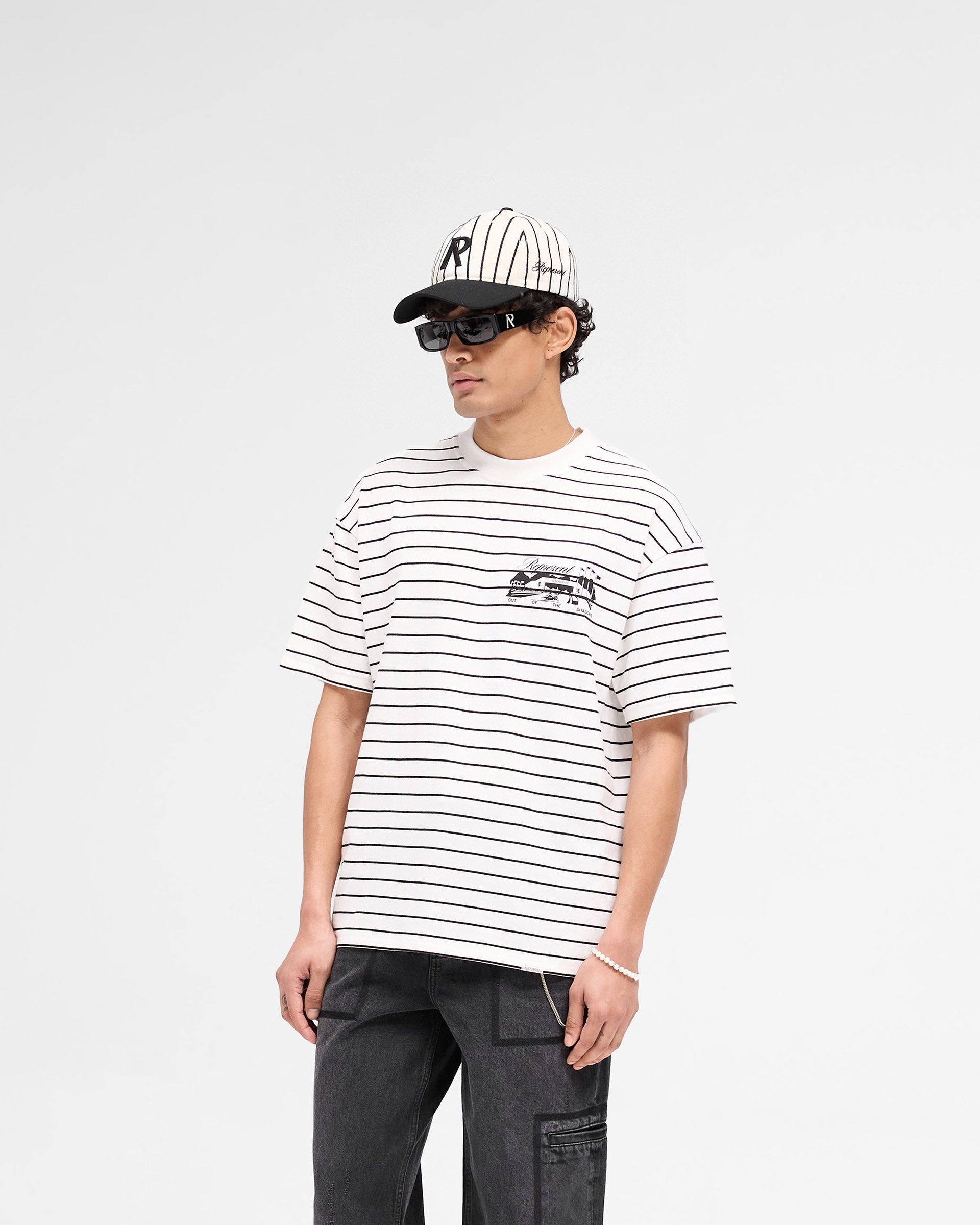 Man wearing a striped t-shirt in matcha on a plain white background | Raceway T-Shirt in Stripe | Slightly oversized t-shirt with puff print graphic | SS25 T-Shirts | Represent Clo