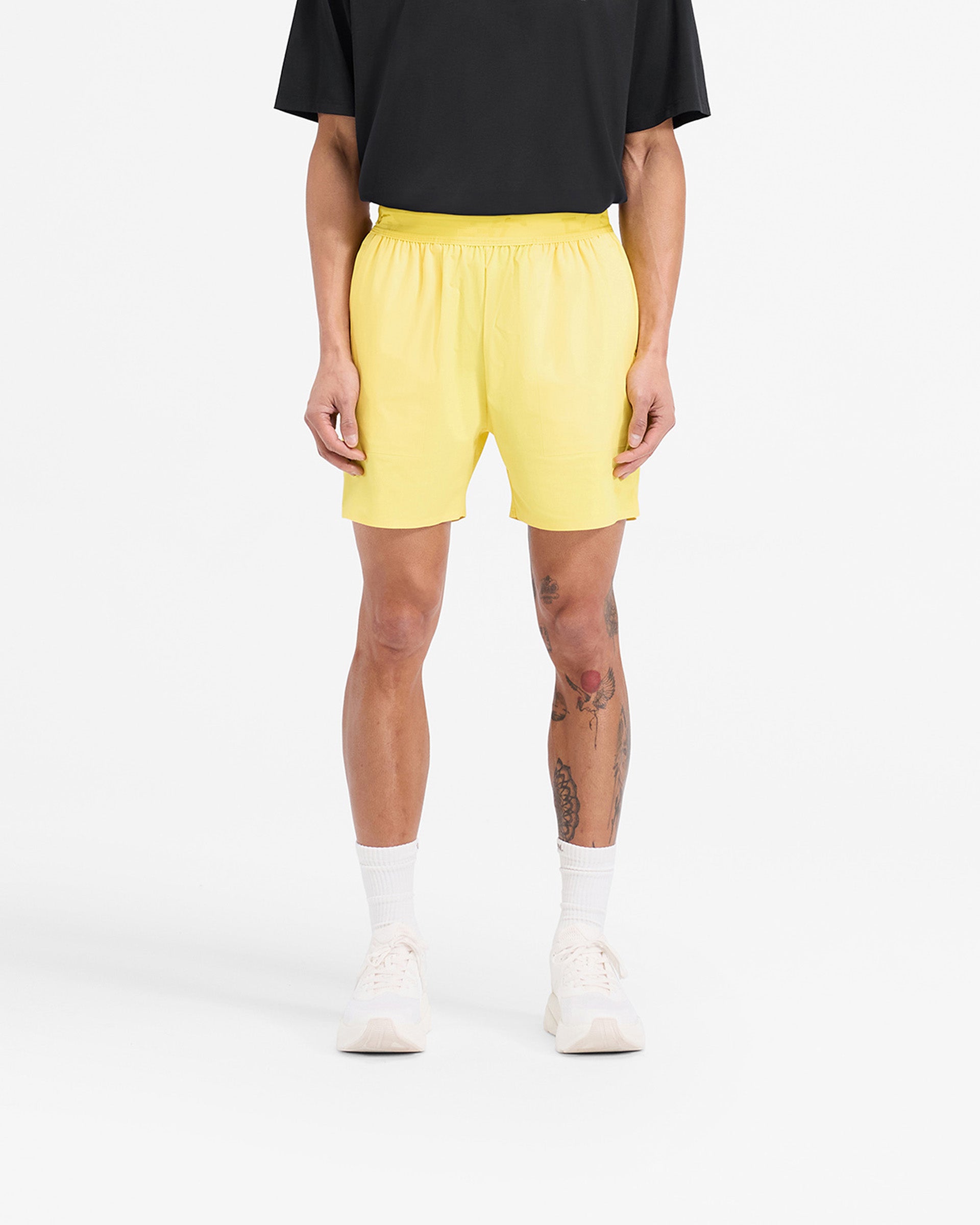 Man wearing yellow training shorts on a plain white background | Team 247 Fused Shorts in Lemon | Gym shorts with internal drawcords and quick drying fabric | 247 Shorts | Represent Clo