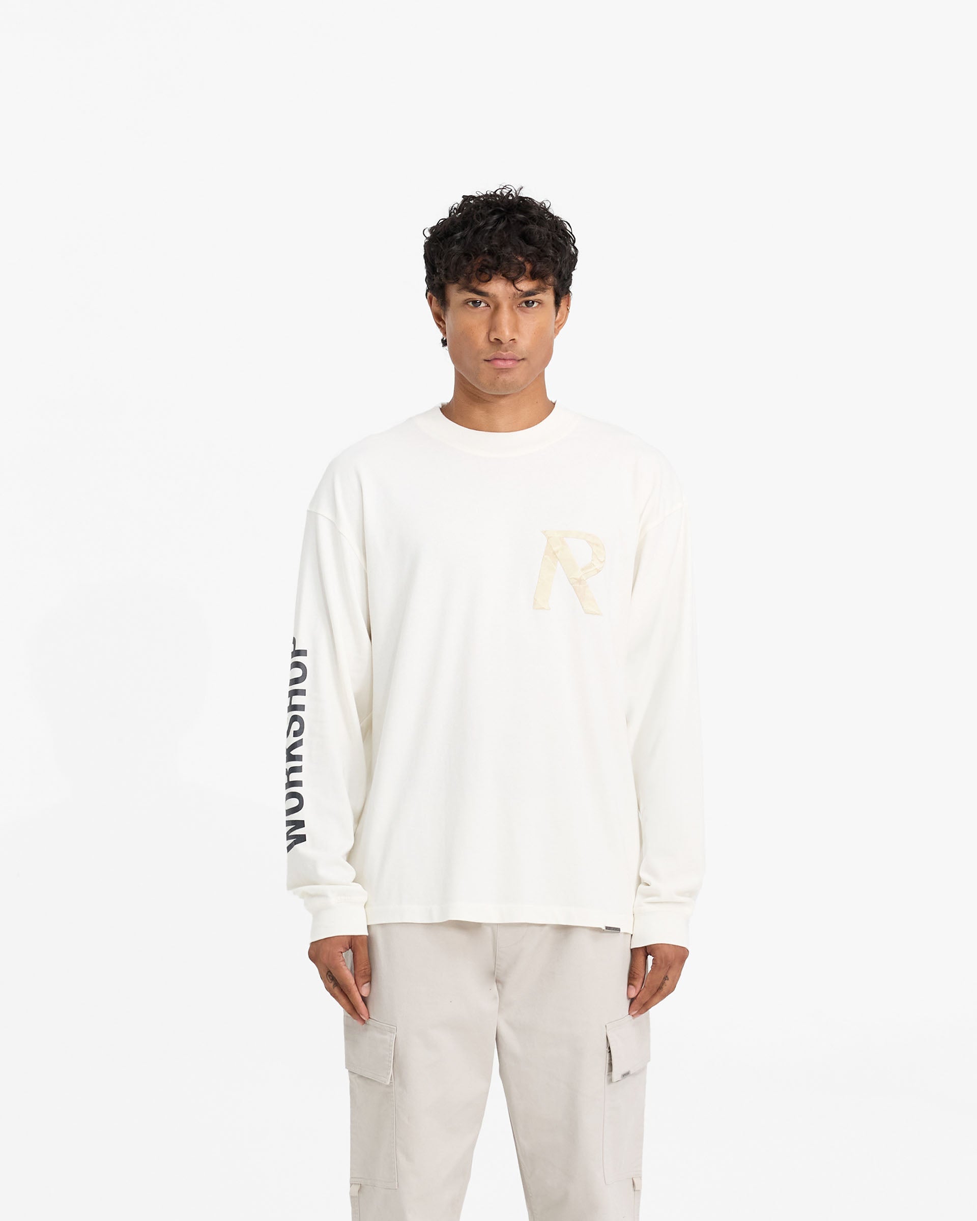 Man wearing a white long sleeve t-shirt on a plain white background | Masking Tape Initial Long Sleeve T-Shirt in Flat White | Slightly oversized t-shirt with 3D masking tape effect | FW24 T-Shirts | Represent Clo