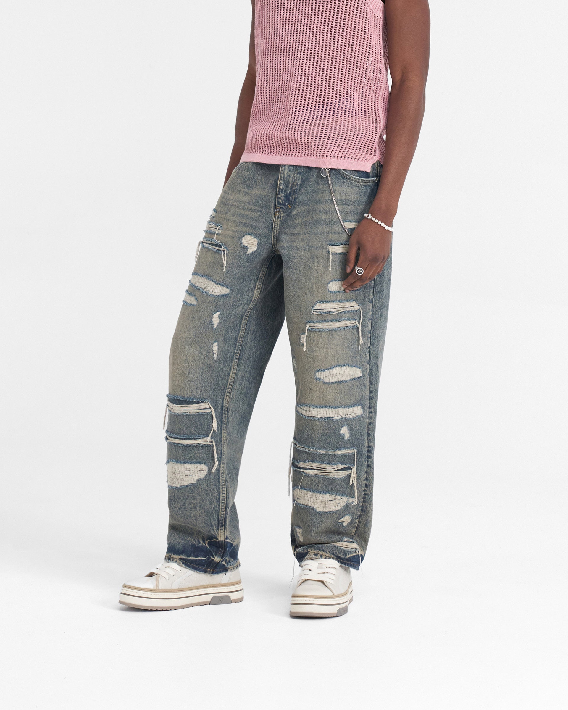 Man wearing blue denim jeans with a heavy distressed look on a plain white background | R3D Double Destroyer Baggy Denim in Blue Cream | Baggy fit jeans with rips and embroidered detail | SS24 Denim | Represent Clo