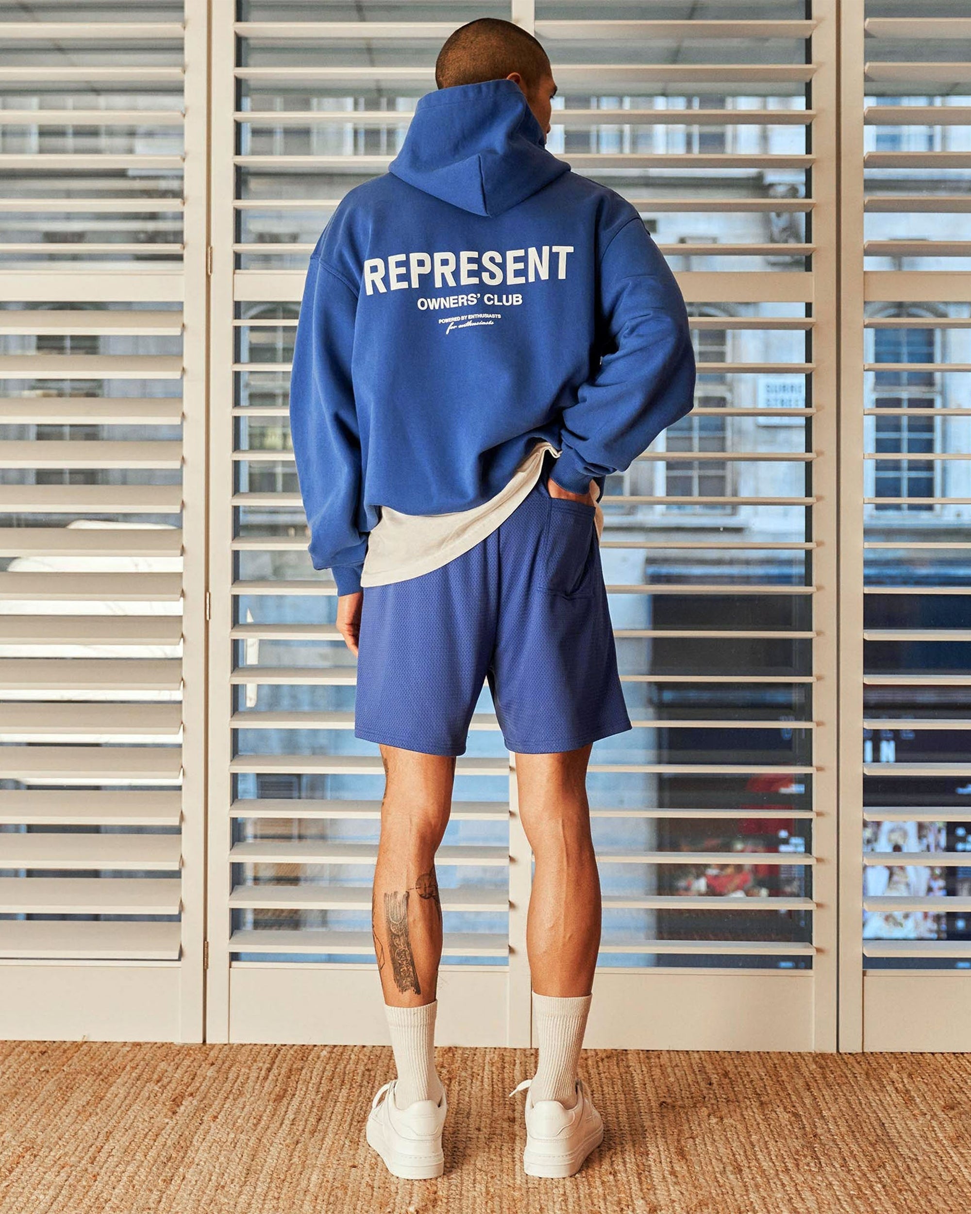 Man wearing cobalt blue mesh shorts on a plain white background | Represent Owners Club Mesh Shorts in Cobalt | Relaxed fit mesh shorts with drawcords | Owners Club Shorts | Represent Clo